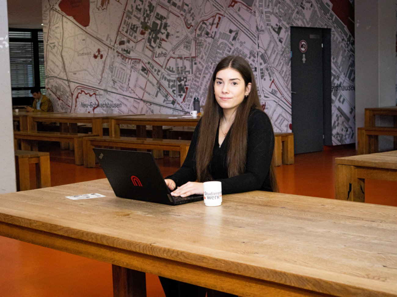 Ayleen sitzt in der Cafeteria im GW2, auf dem Tisch steht ihr Laptop