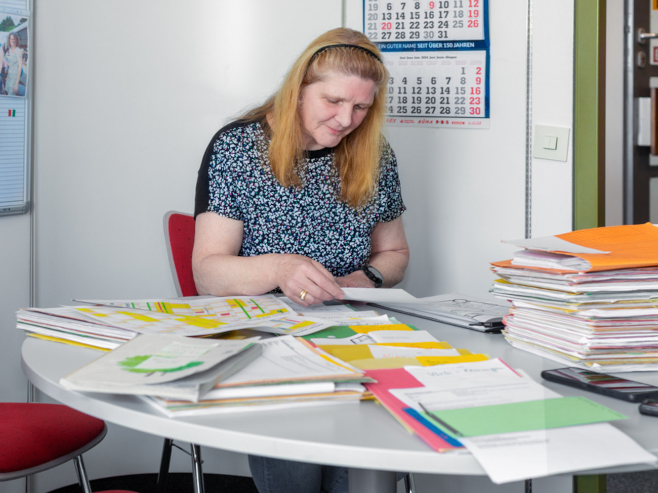 Heike Hemmersbach sitzt an ihrem Schreibtisch zwischen viel Papierkram.