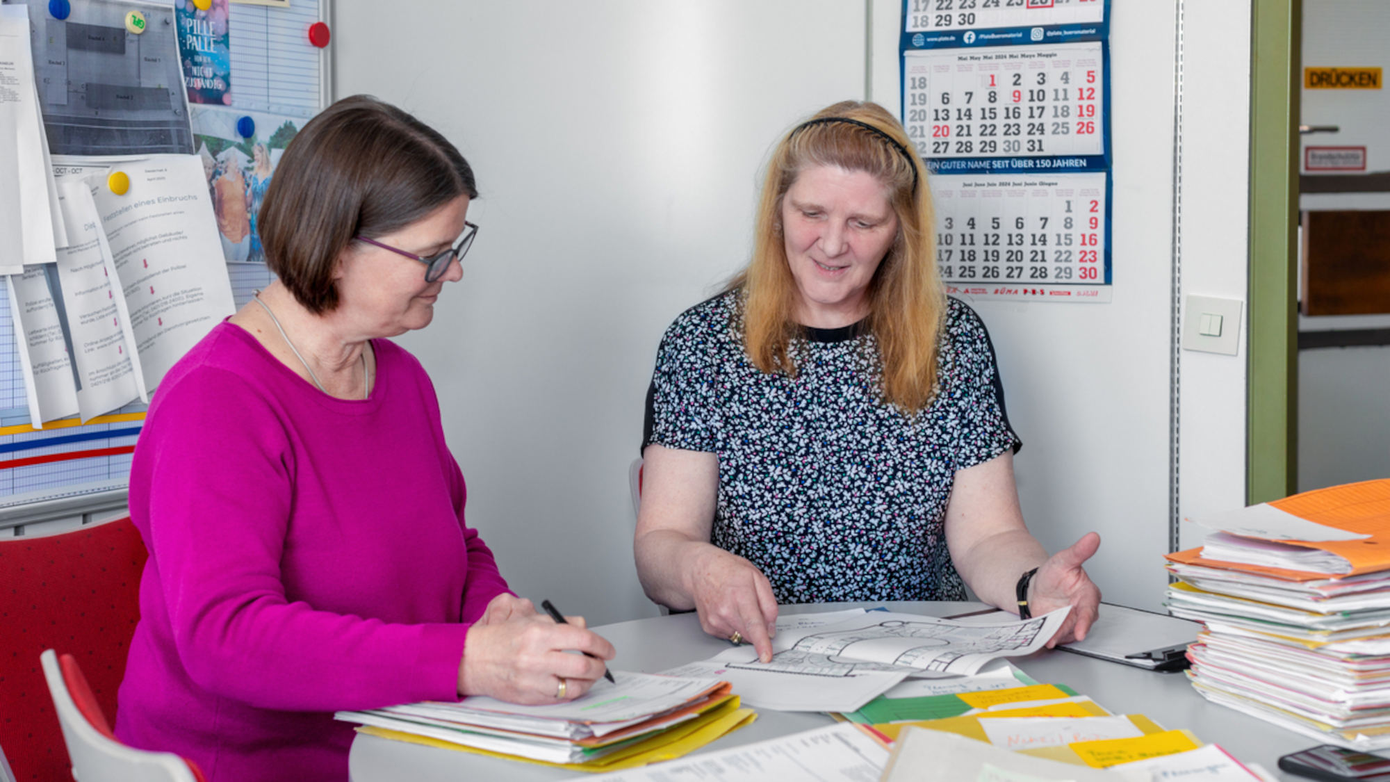 Heike Hemmersbach und Andrea Saathoff sitzen am Schreibtisch, auf welchem viele Papiere zu sehen sind.