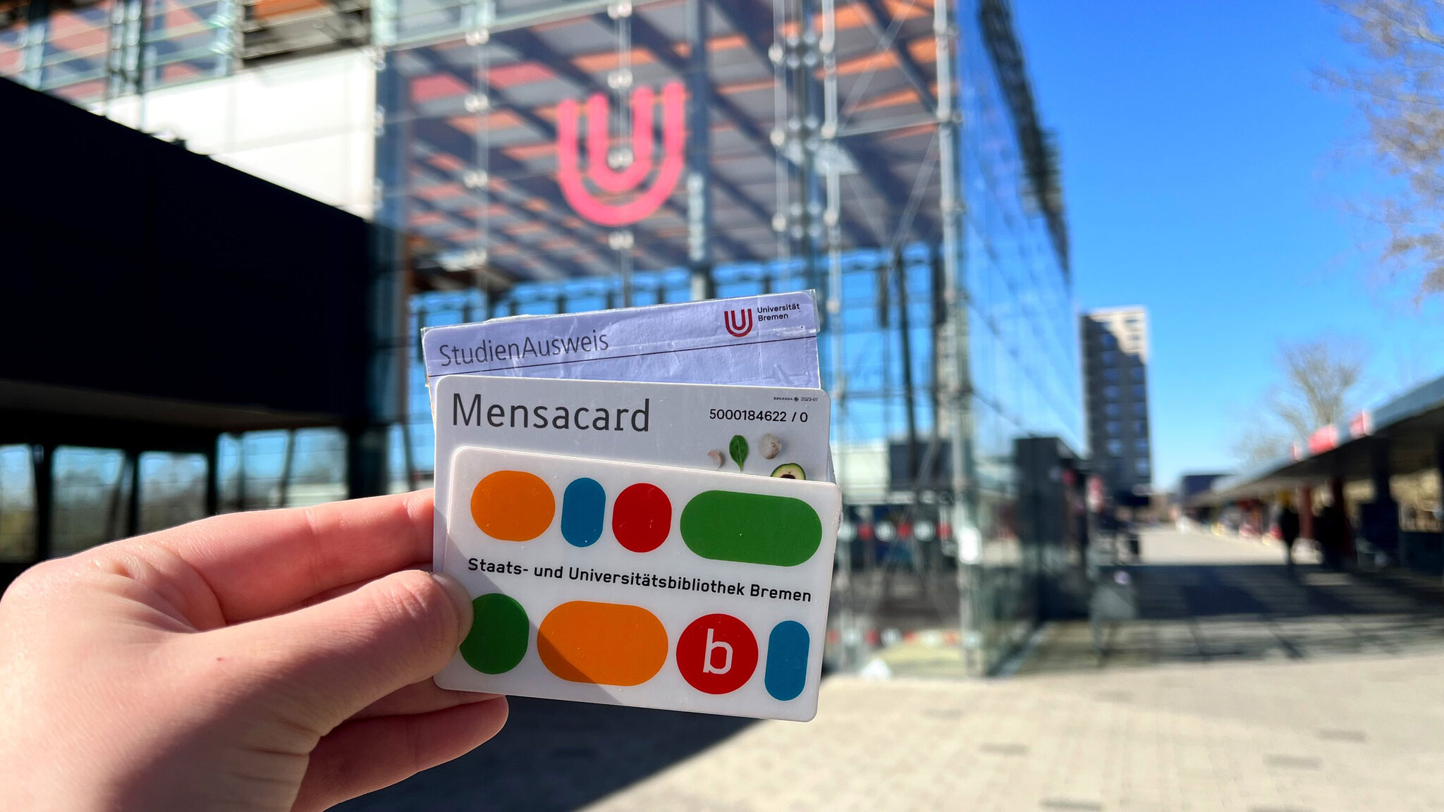 Bibliothekskarte, Mensacard und Studierendenausweis werden von einer Hand gehalten.