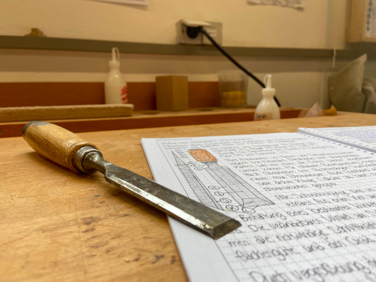 Sarah's report booklet is lying on a table with a chisel on top.