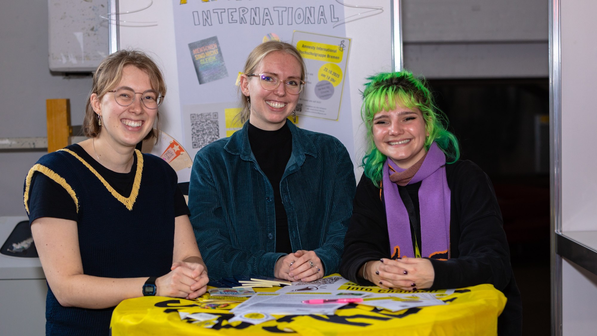 Three people are standing at a bar table and are smiling at the camera. 