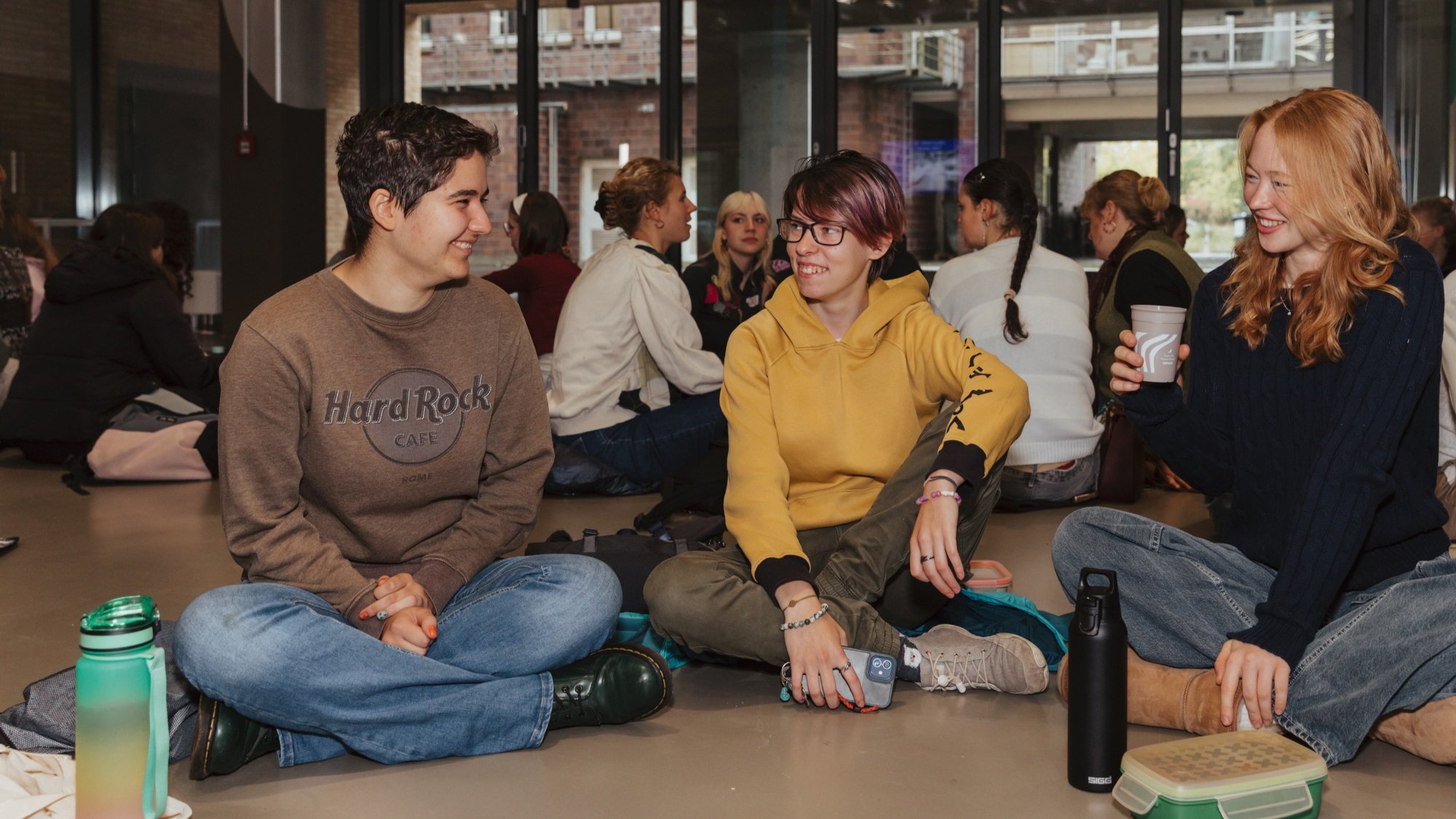 Three students are sitting on the floor and are laughing together.