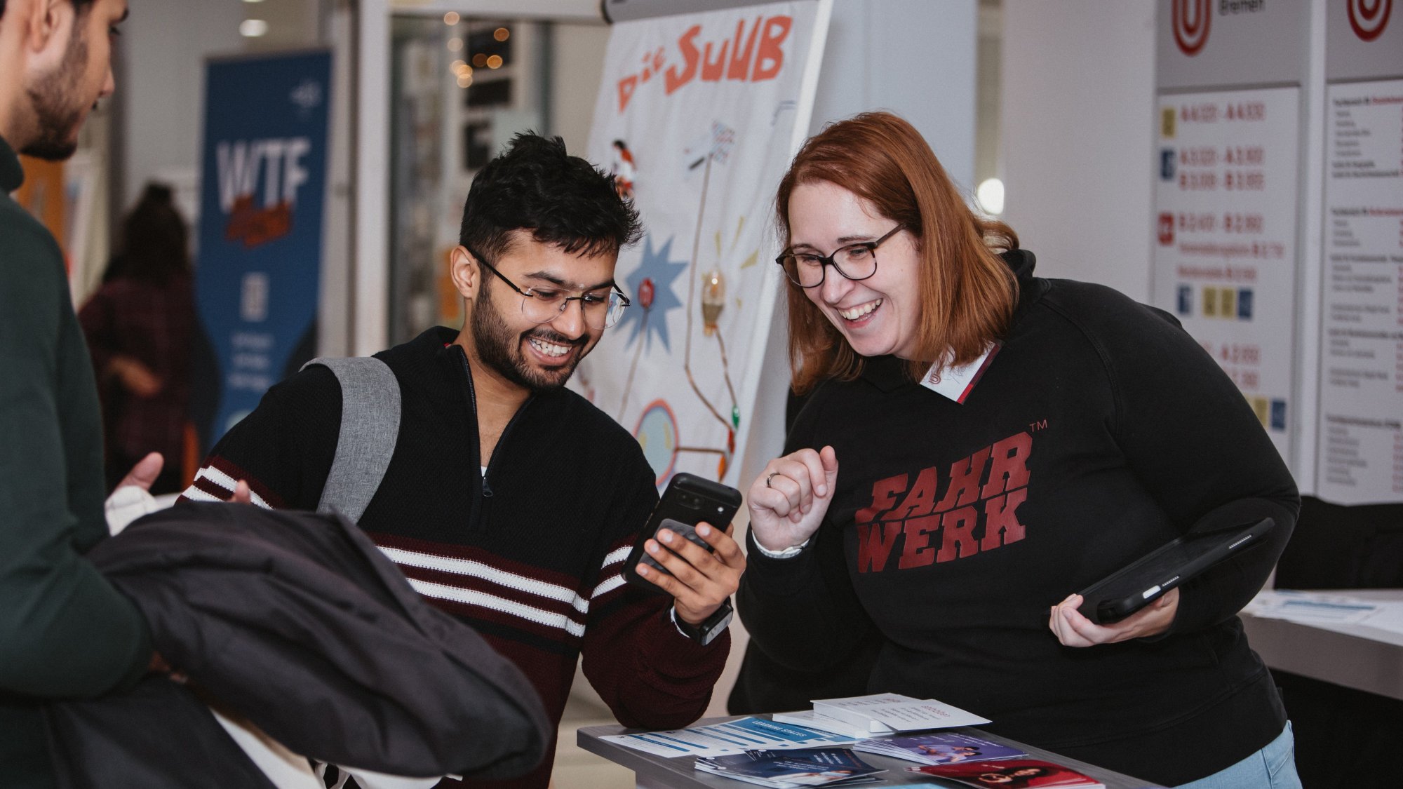 Two people are looking at a smartphone at an information stand. 
