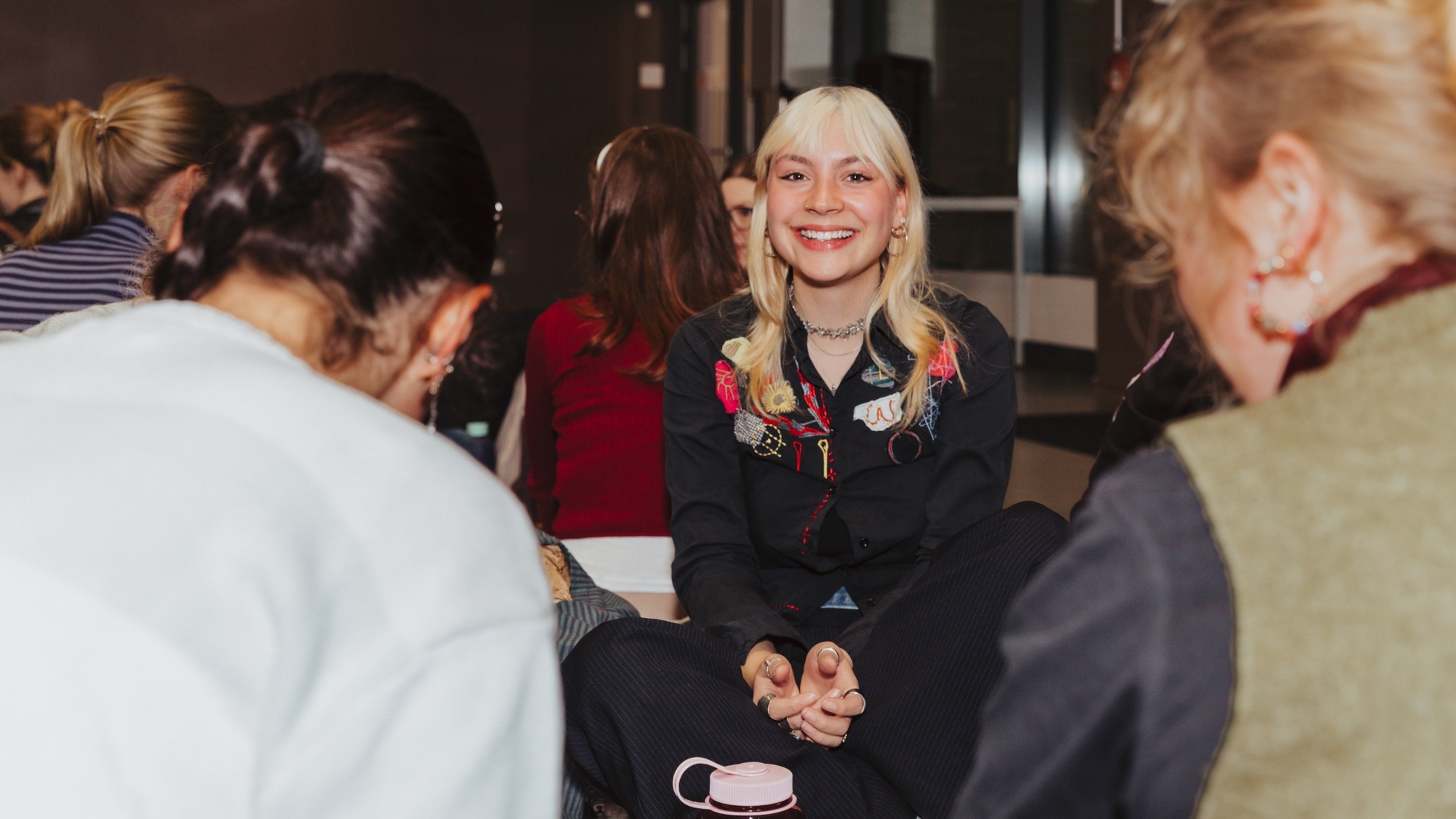 A woman is sitting on the ground and is smiling at the camera. 