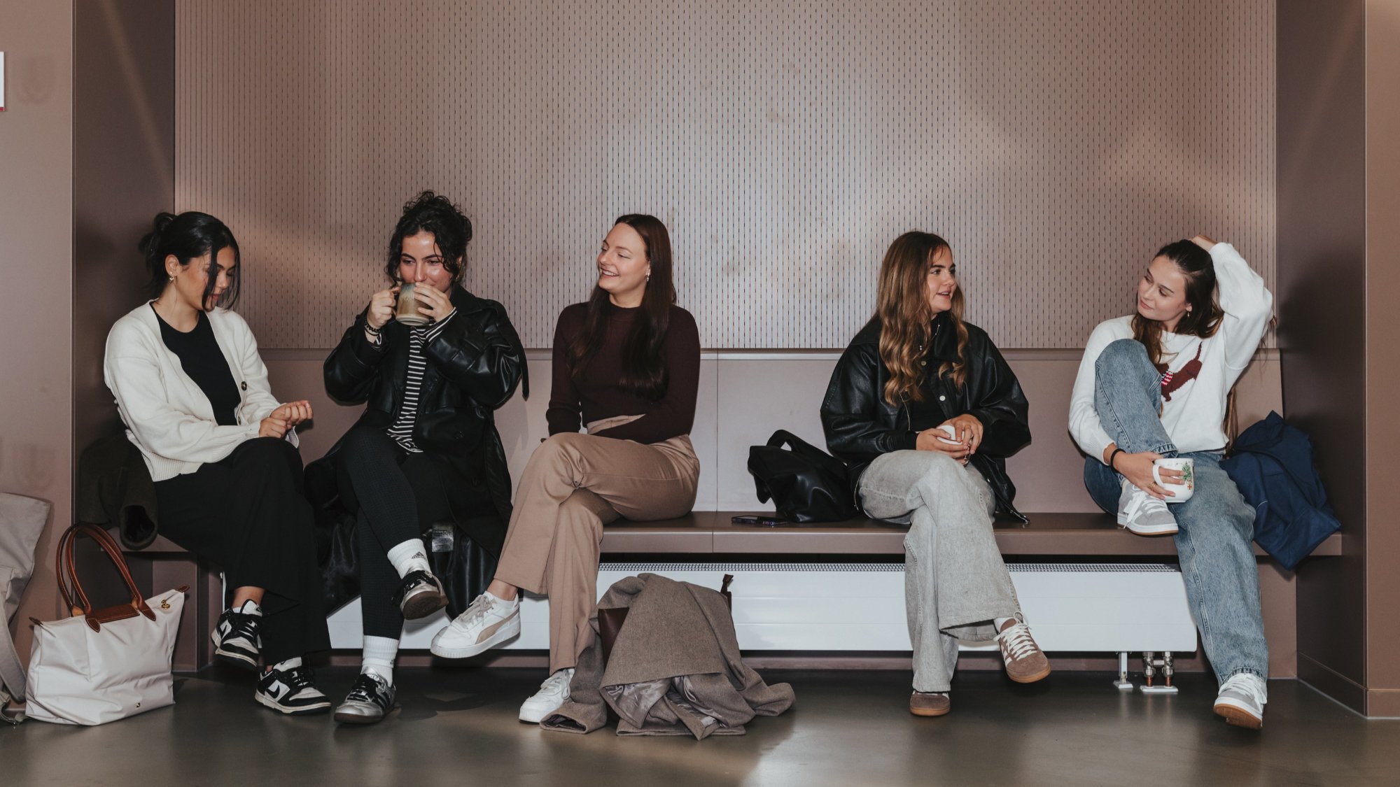 Five people are sitting on a sofa against the wall and are chatting. 