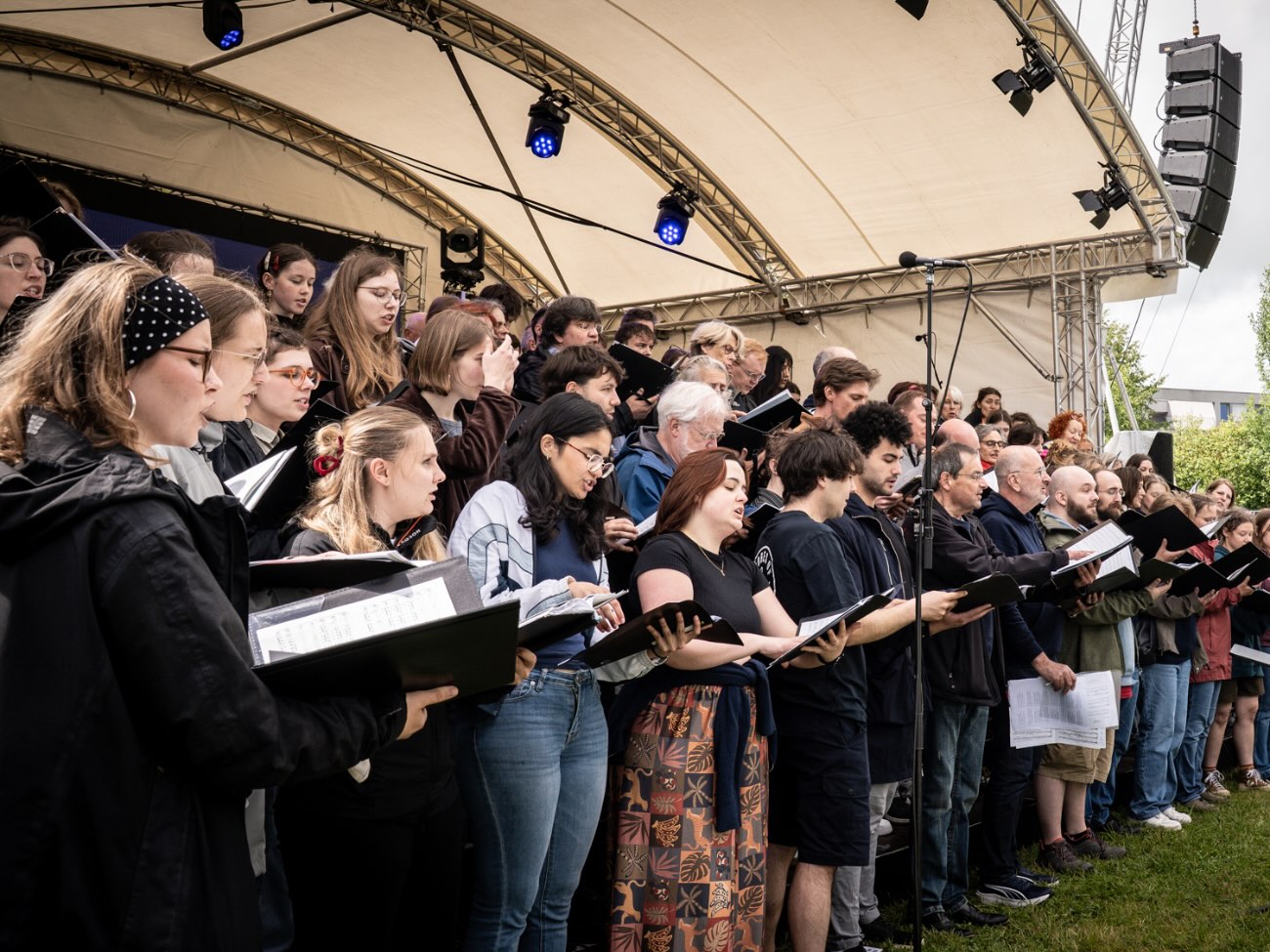 The choir members stand in rows and sing while holding their music folders. 