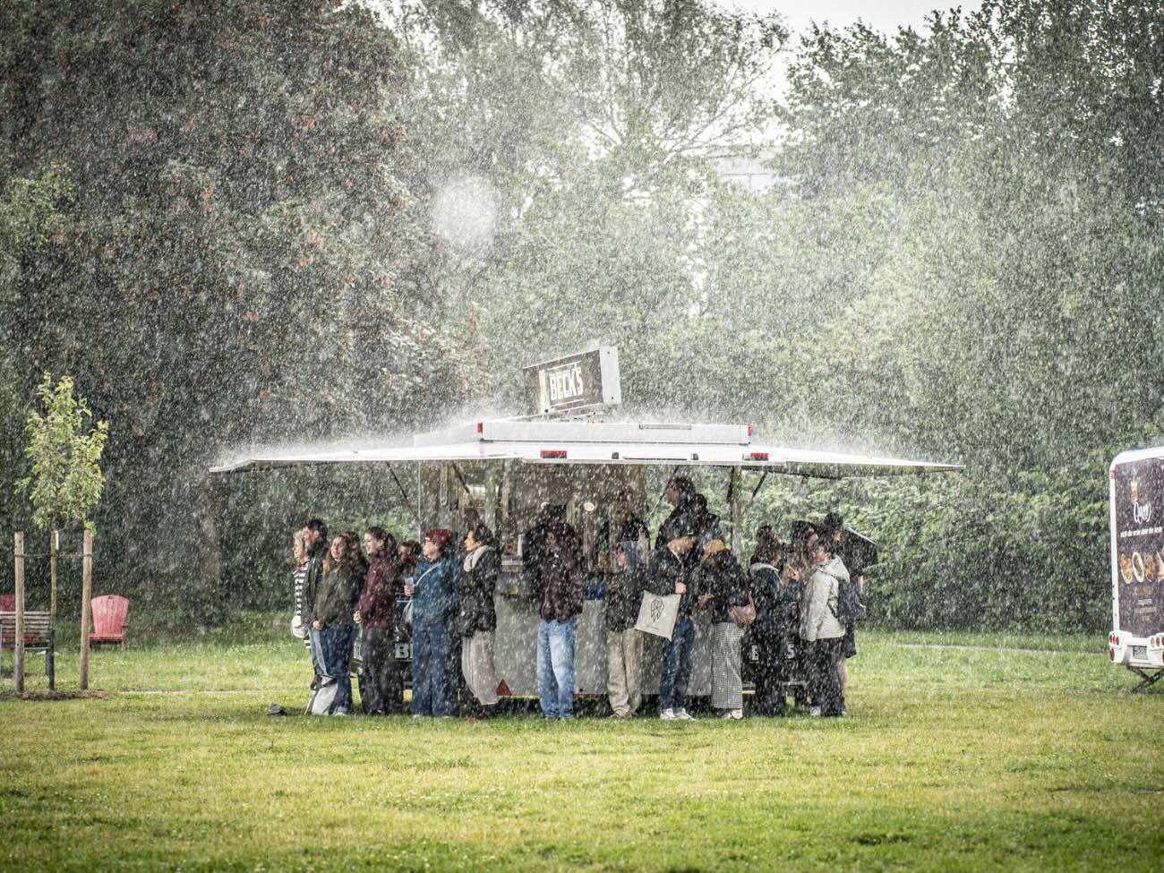 The participants are standing under the shield of the outdoor beer kiosk. 
