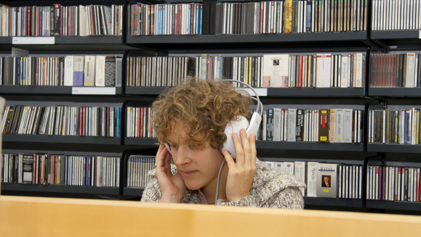 Mann sitzt mit Kopfhörern vor einem CD-Regal