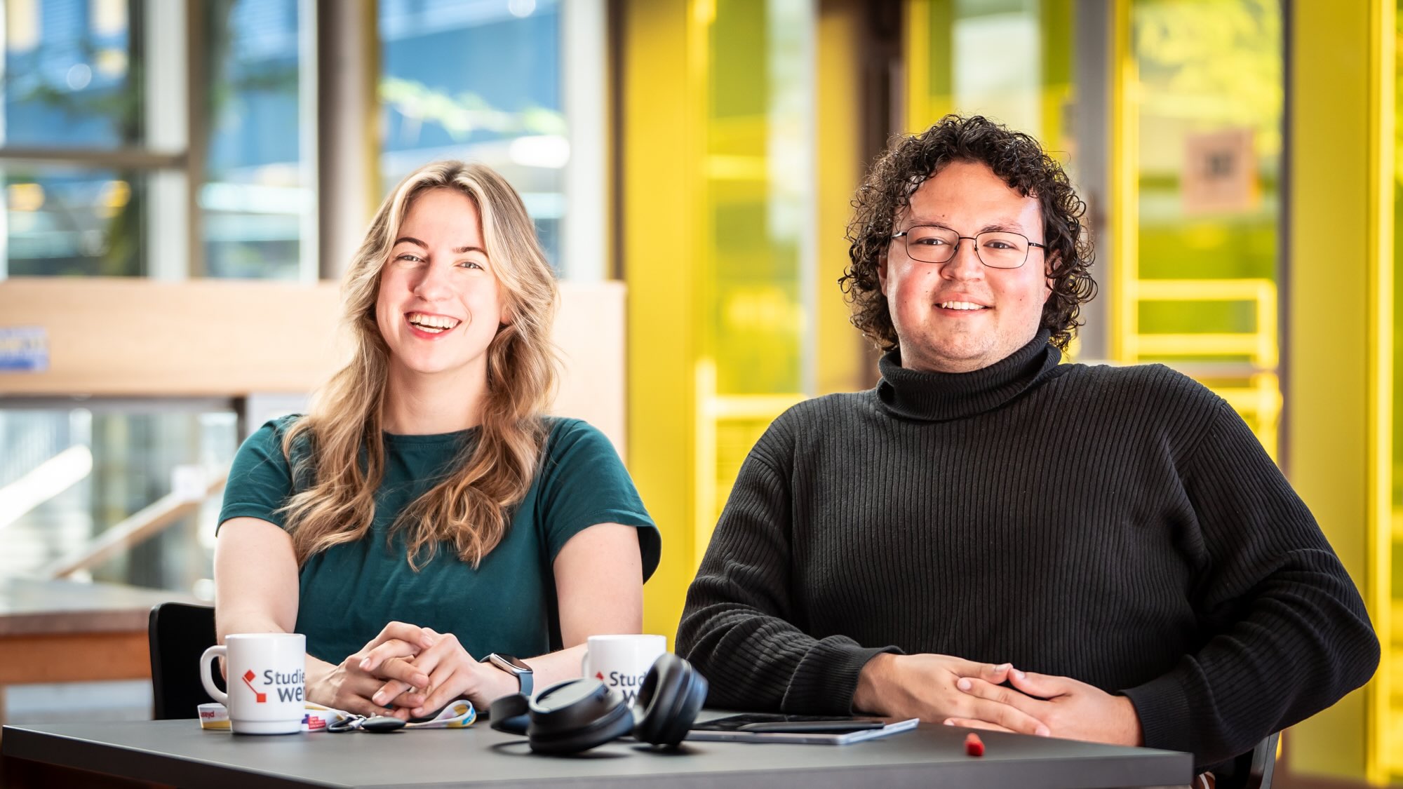 Paulina and Deniz are sitting next to each other at a table and smiling at the camera.