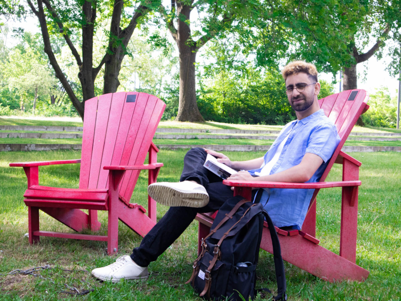 Zakir sitzt auf einem der roten Dickinson-Stühlen auf der Uniwiese.