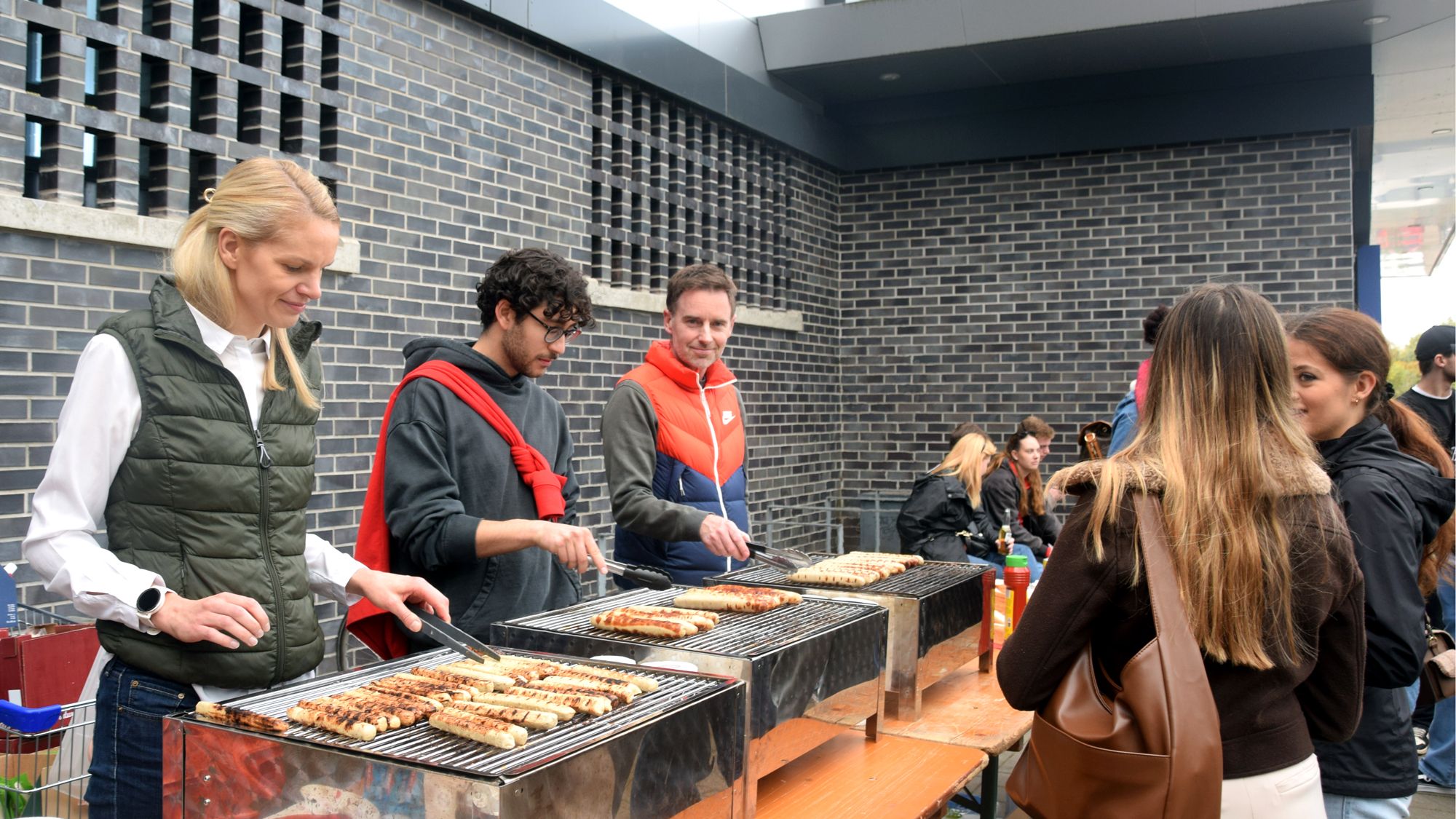 Three people are standing behind the grills, turning the food.