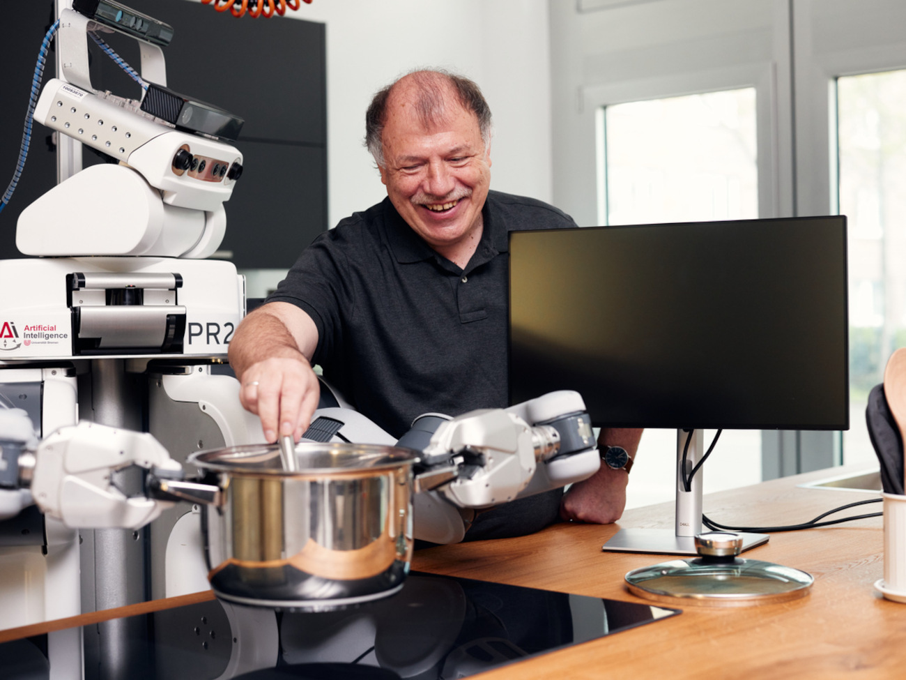 Michael Beetz rührt in einem Topf, den ein Roboter festhält.