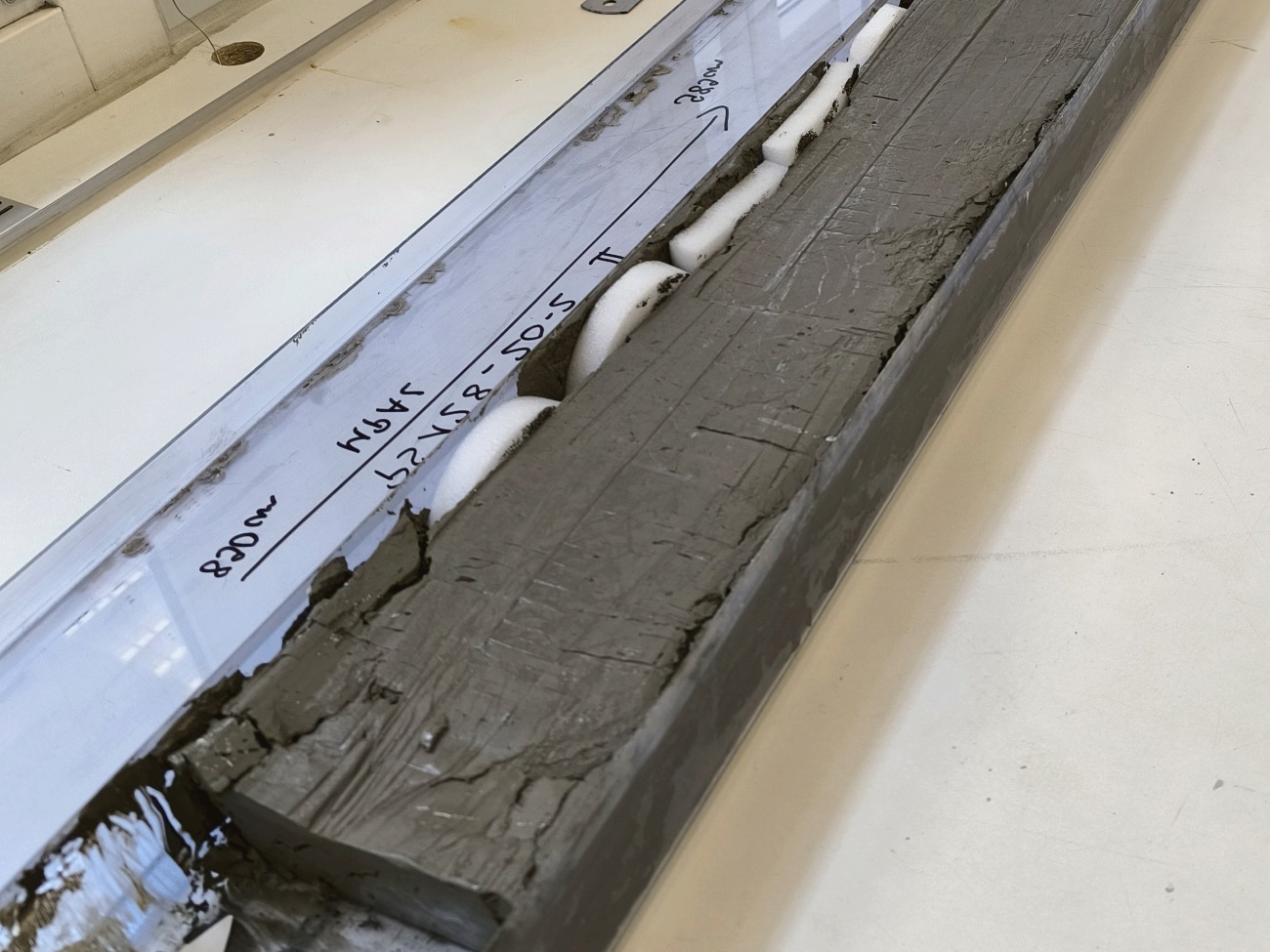 The image depicts a black, elongated block next to a plastic strip.
