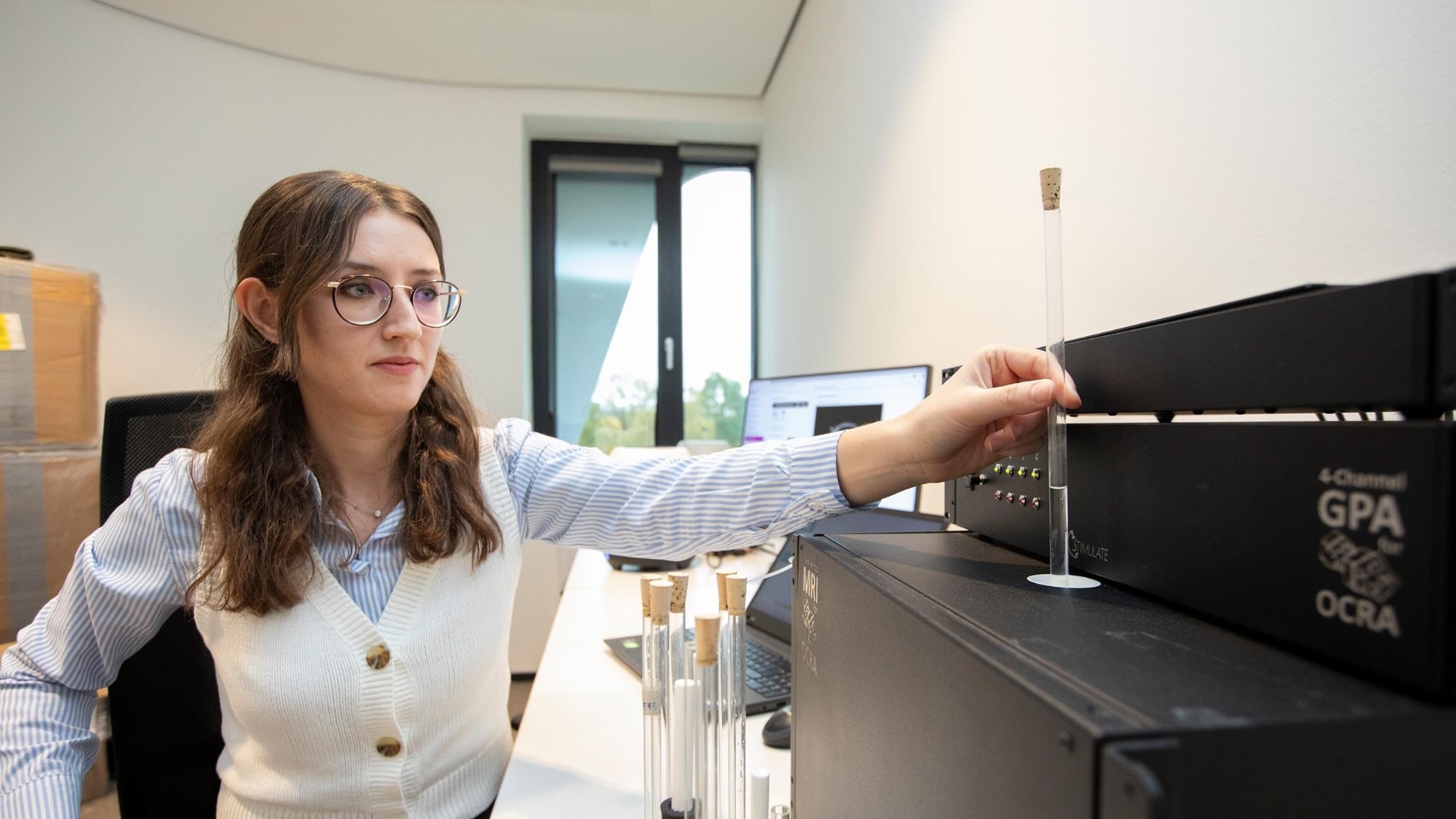 Eine Person hält in einem Büro ein teils mit Flüssigkeit gefülltes Reagenzglas