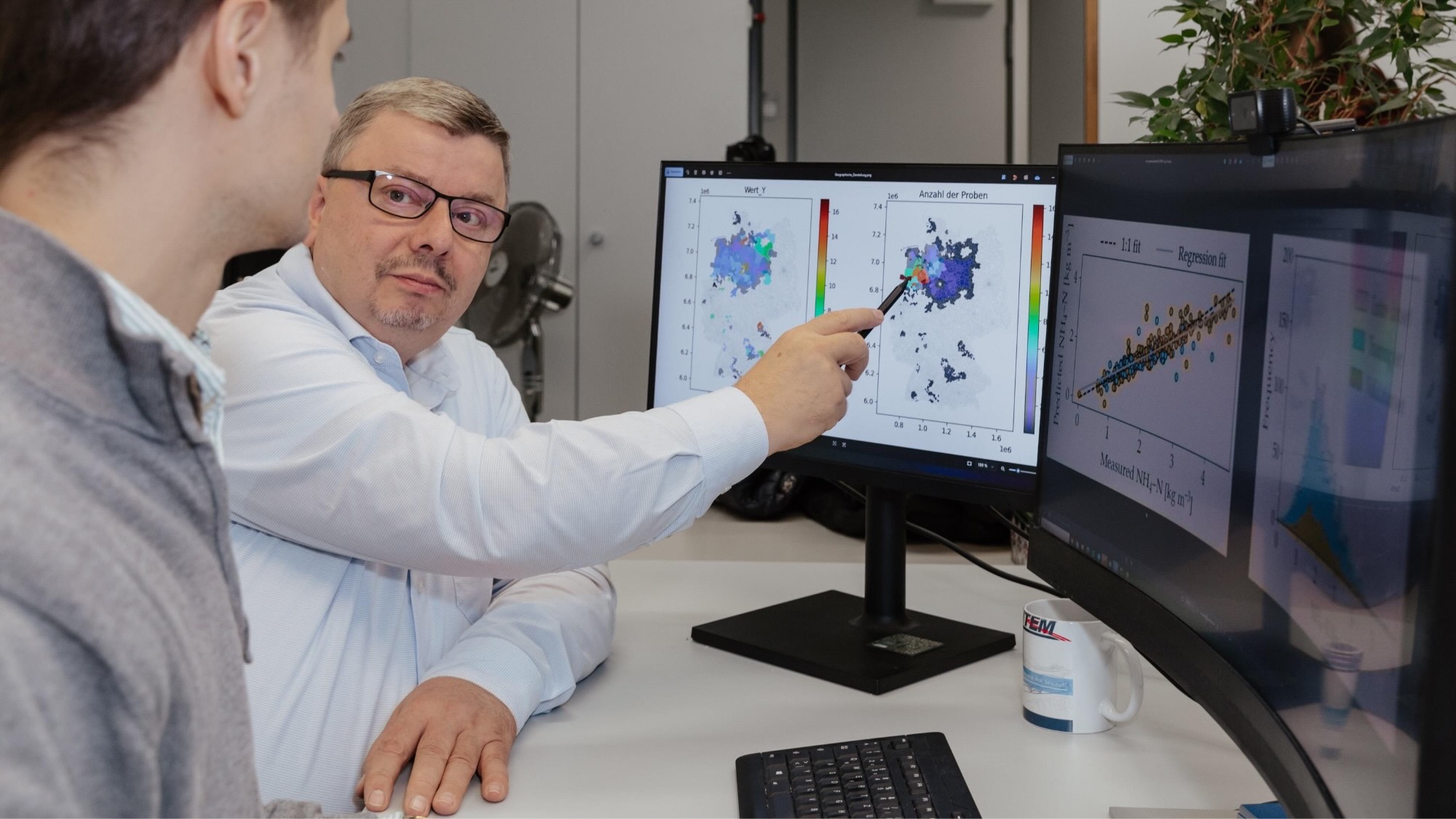 One person shows another person measurements on one of the two screens facing them.  