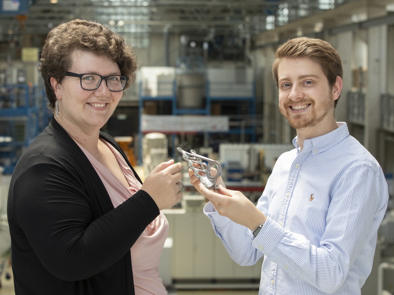Two people are standing opposite each other, holding an object in their hands and smiling at the camera.
