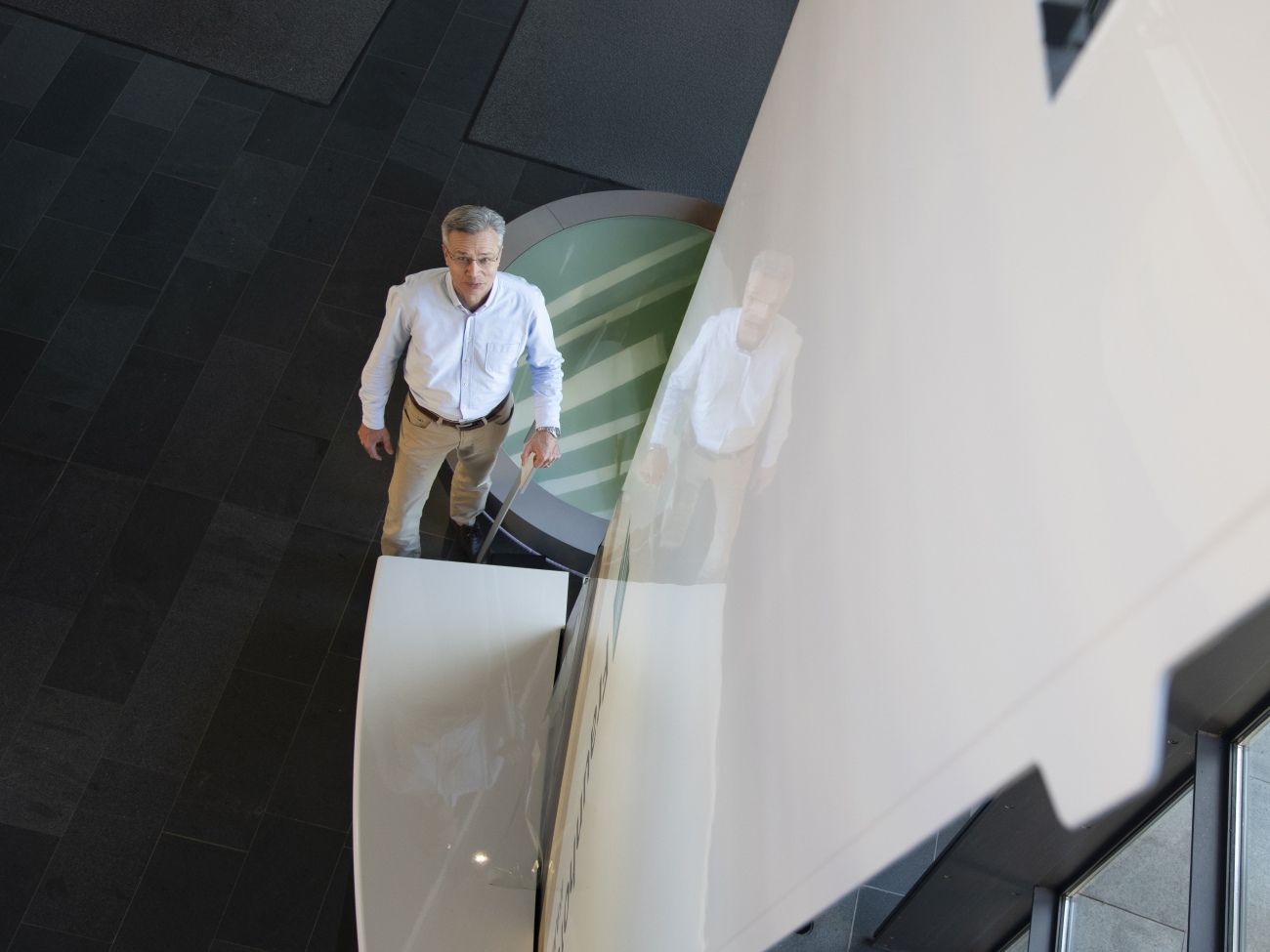 From a bird's eye view, a man can be seen walking alongside a reflective wall. 