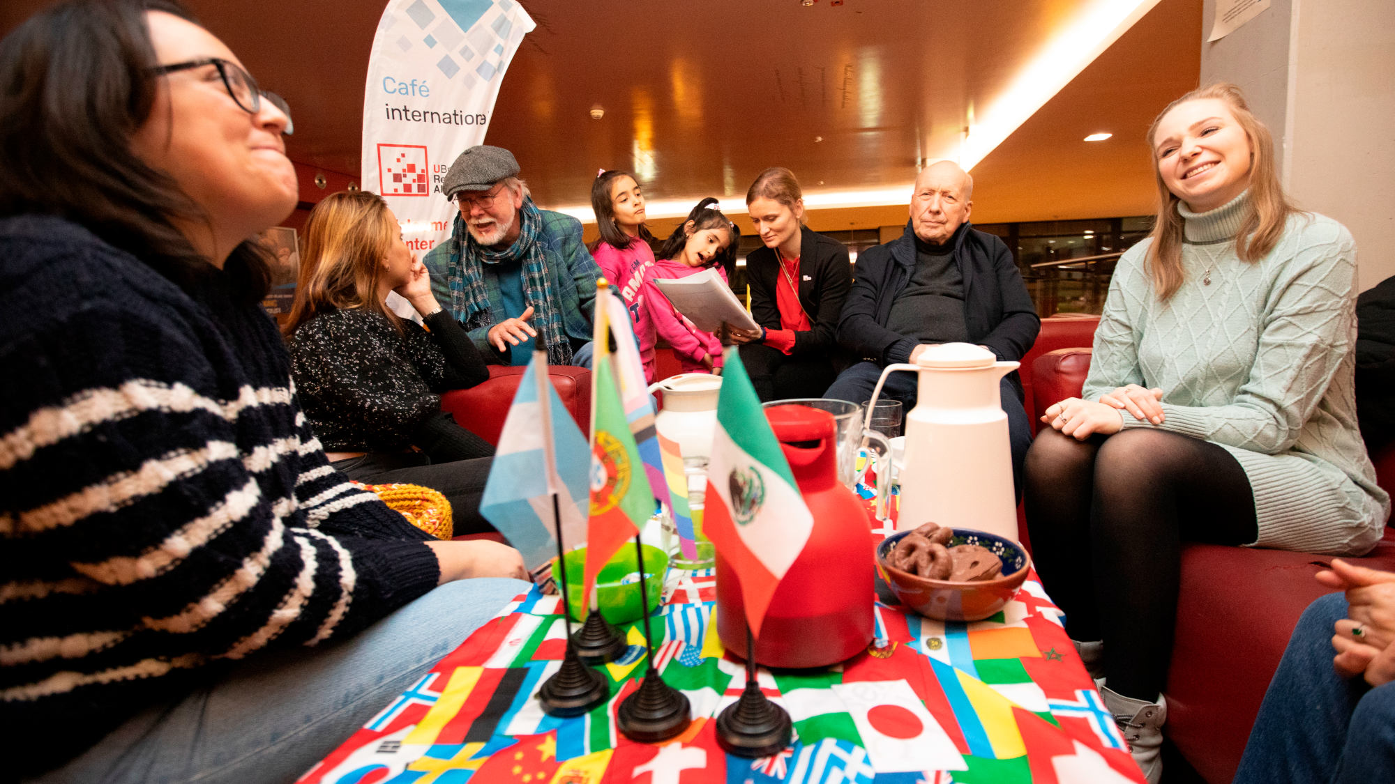 Acht Personen, darunter zwei Kinder, sitzen auf roten Sofas im