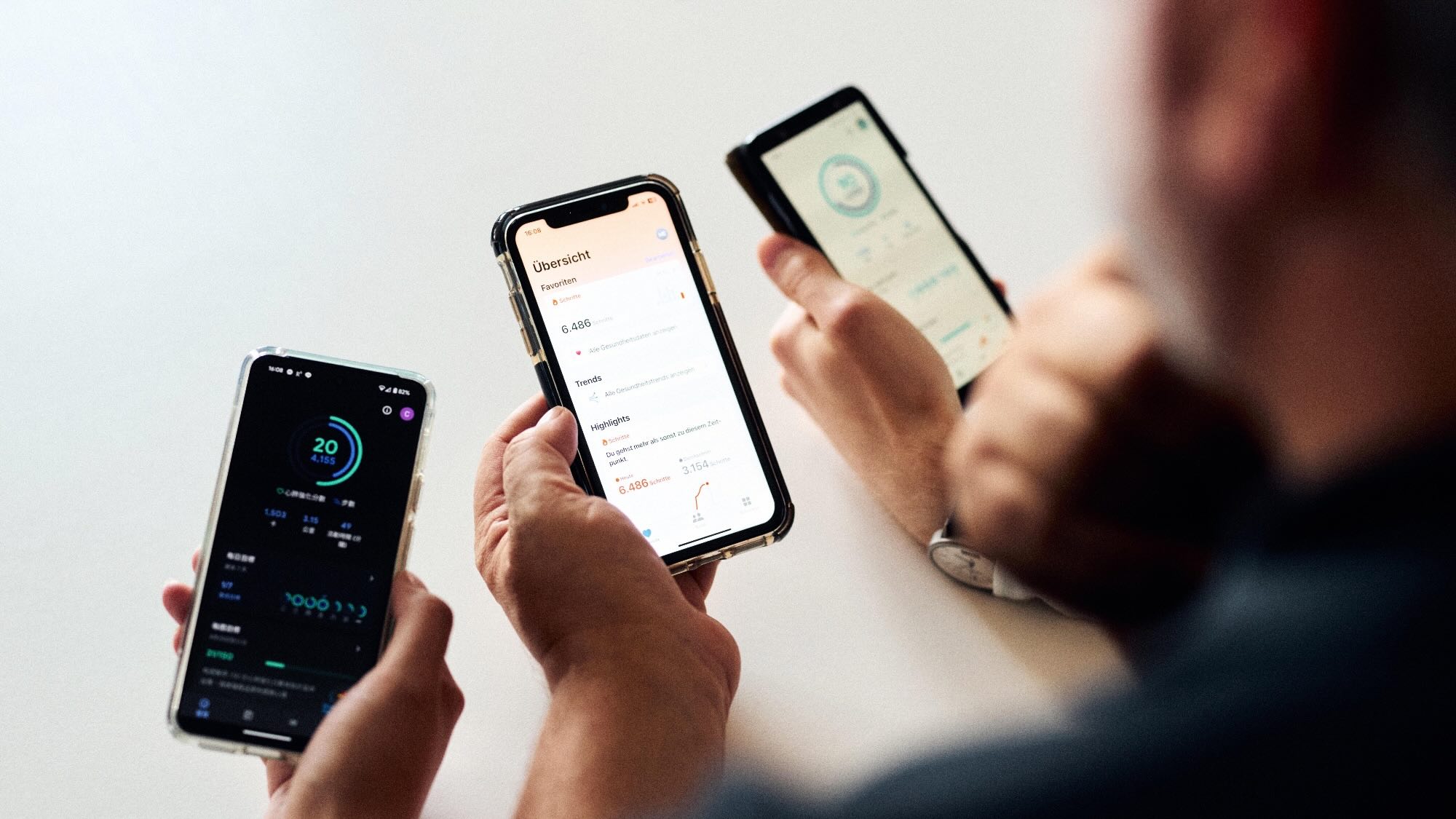 Ein Bild von drei Händen, die jeweils ein Smartphone halten. Die Bildschirme der Smartphones zeigen Fitness-Tracker-Apps.
