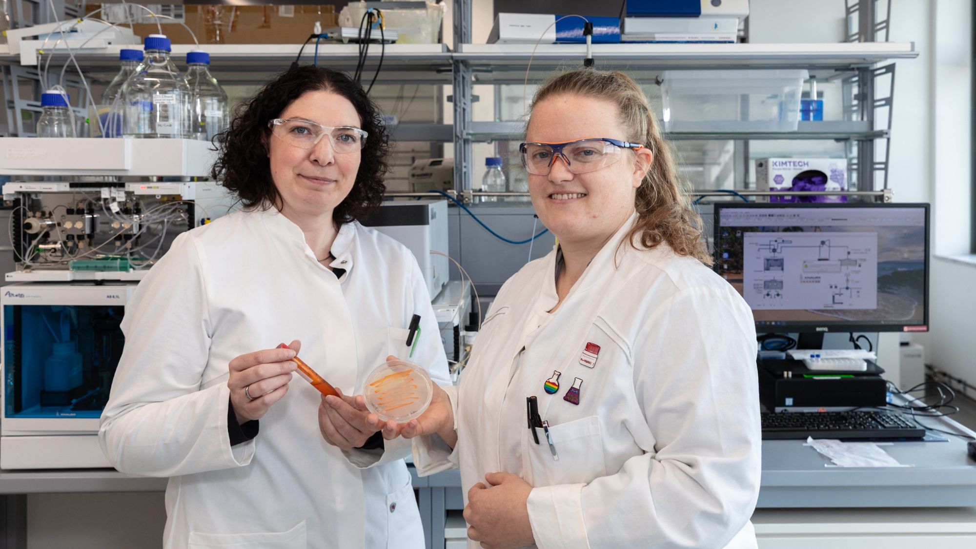 Zwei Frauen stehen in einem Labor und lächeln in die Kamera.