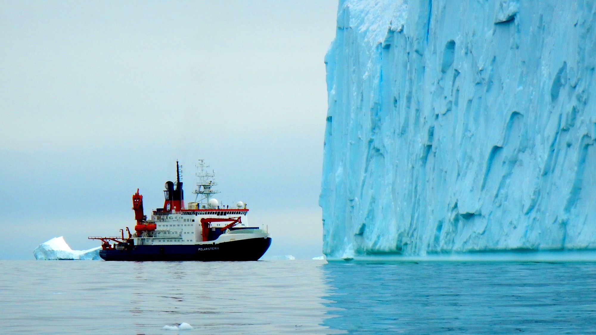Ein Schiff fährt an einem Eisberg vorbei.