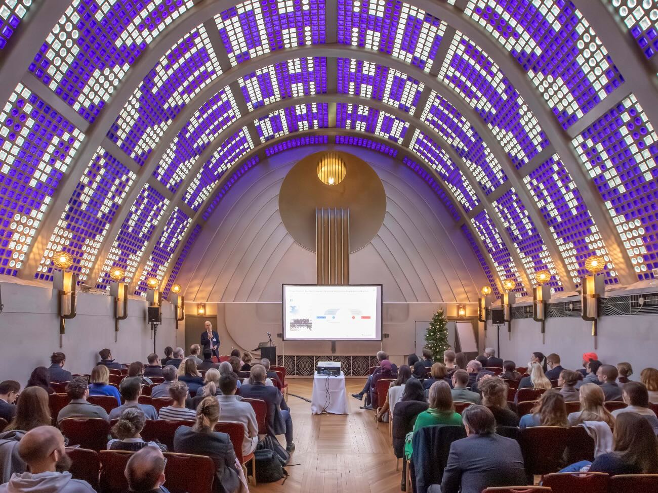 People are sitting in a large hall listening to a lecture.