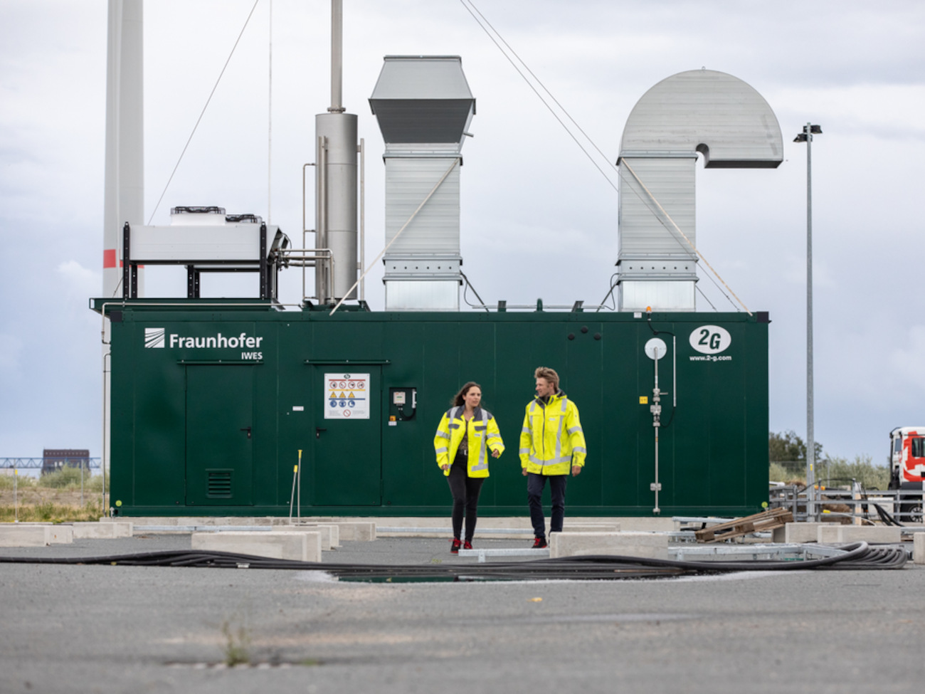 Two people that are wearing yellow safety vests in front of the combined heat and power plant