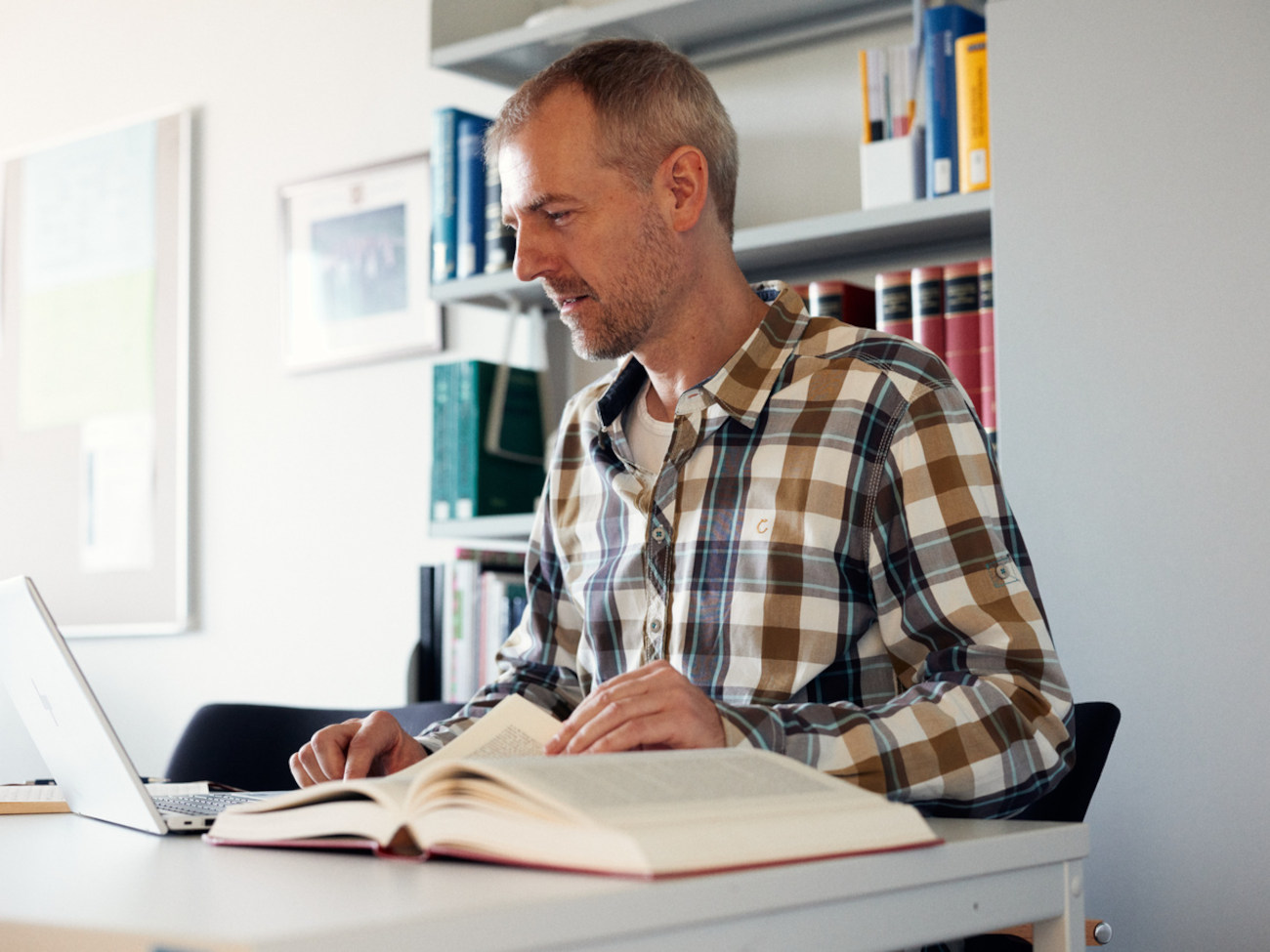 Norman Sieroka sitzt am Schreibtisch vor einem Laptop und einem aufgeschlagenen Buch.