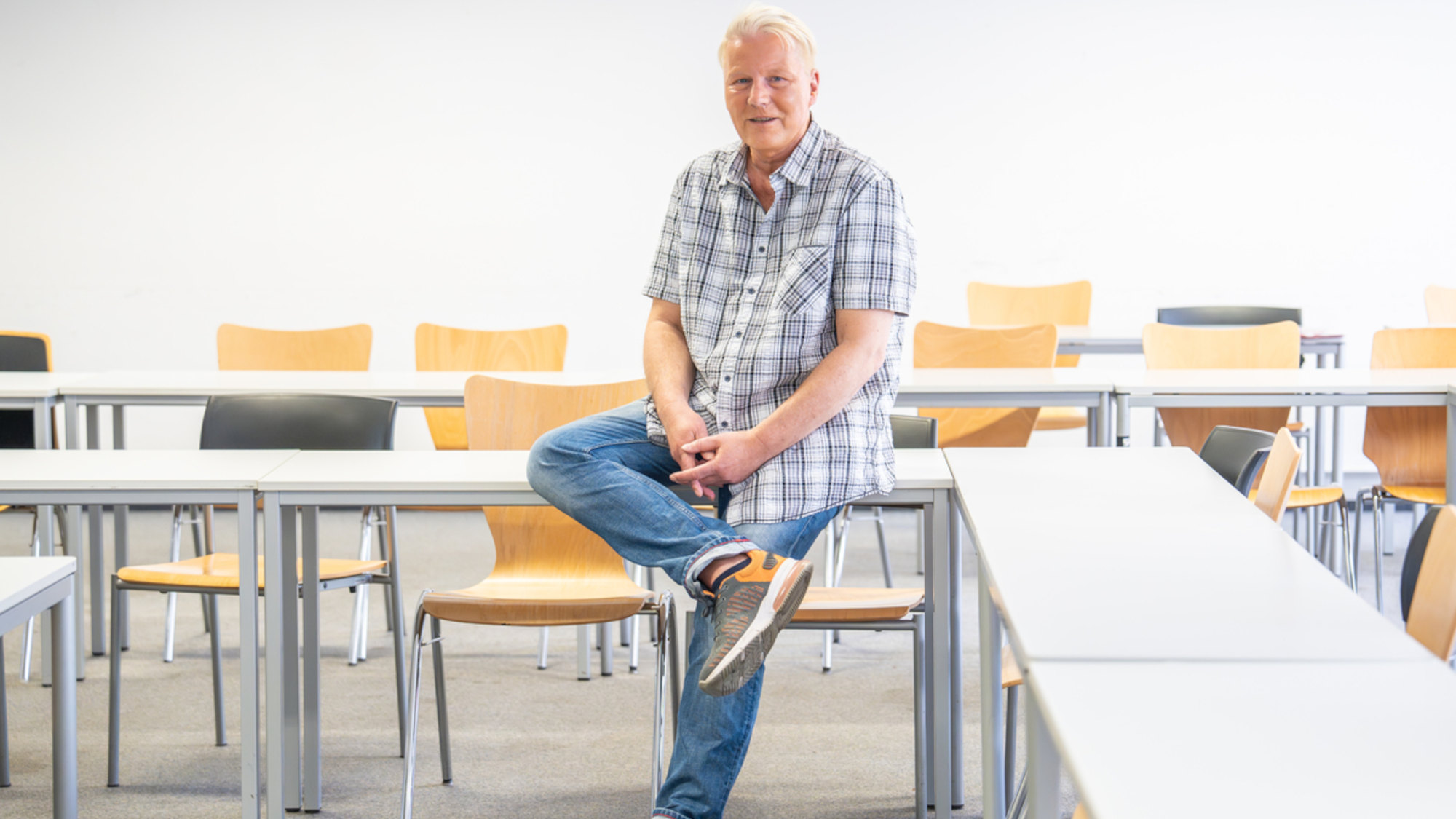 Christian Palentien sitzt in einem Lehrraum auf einem Tisch