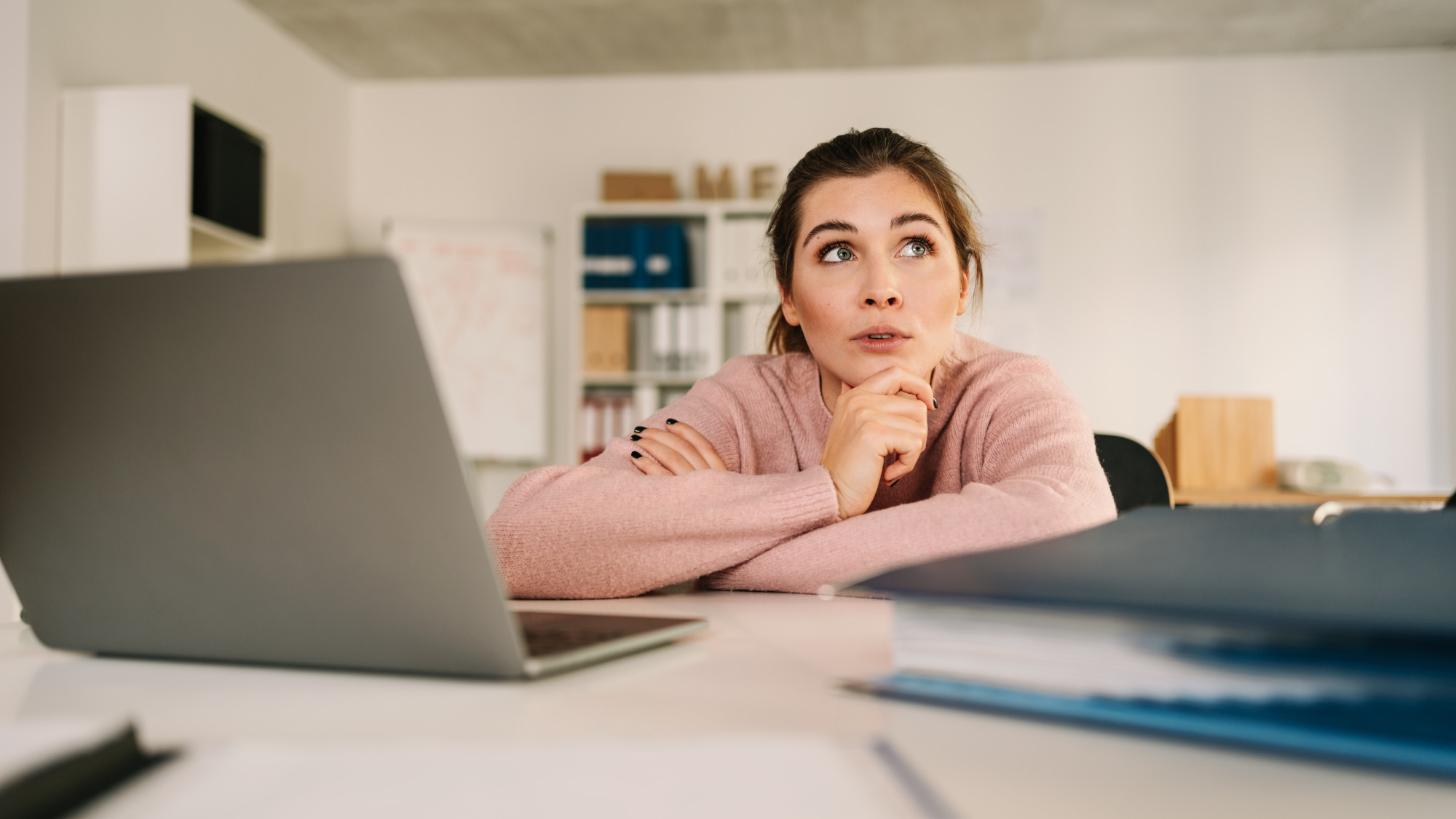 A woman sits in front of her laptop in a pensive pose.