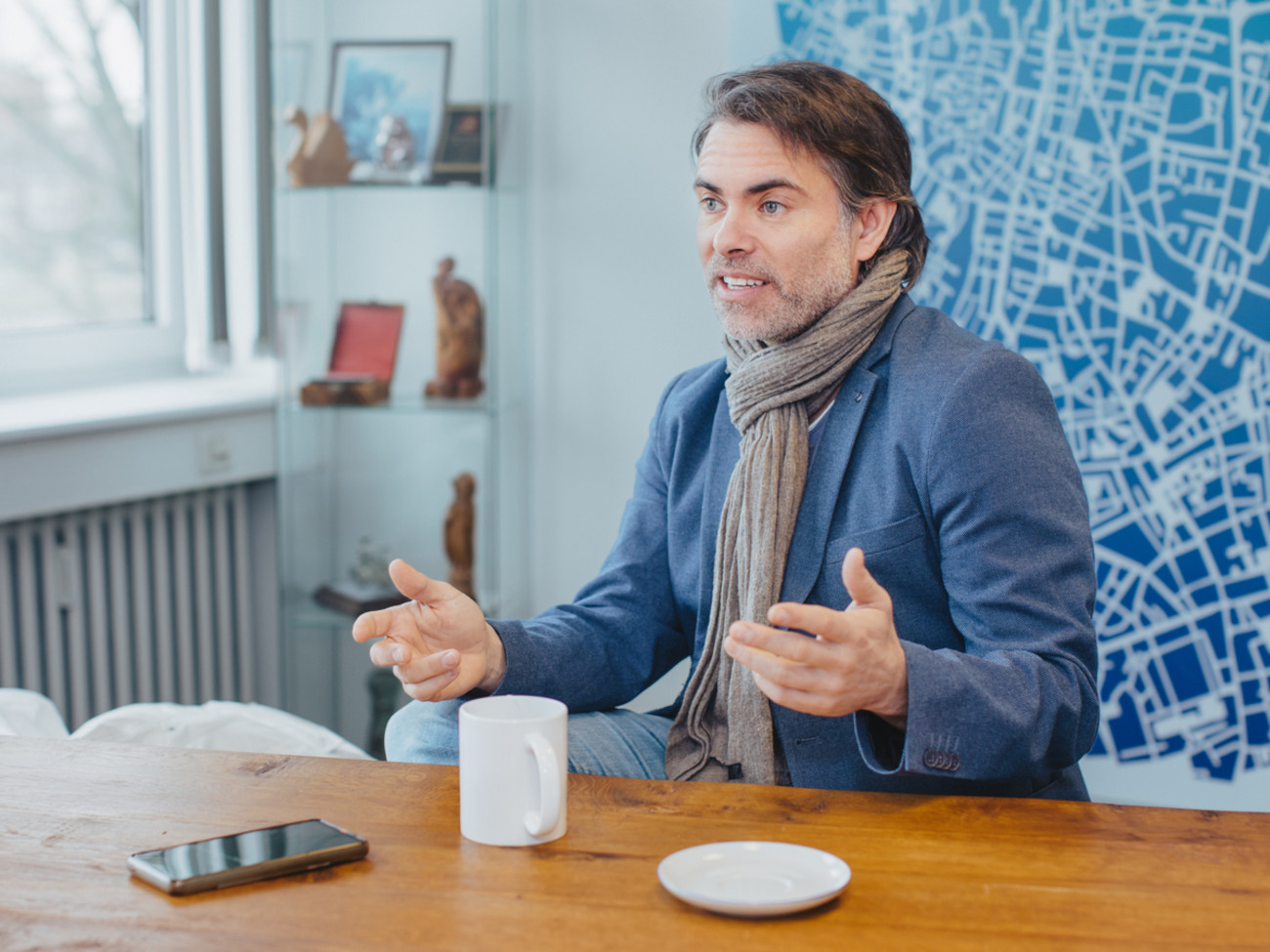 Alexander Wolf is sitting at a table with a cup in front of him. He gestures with his hands as he speaks.