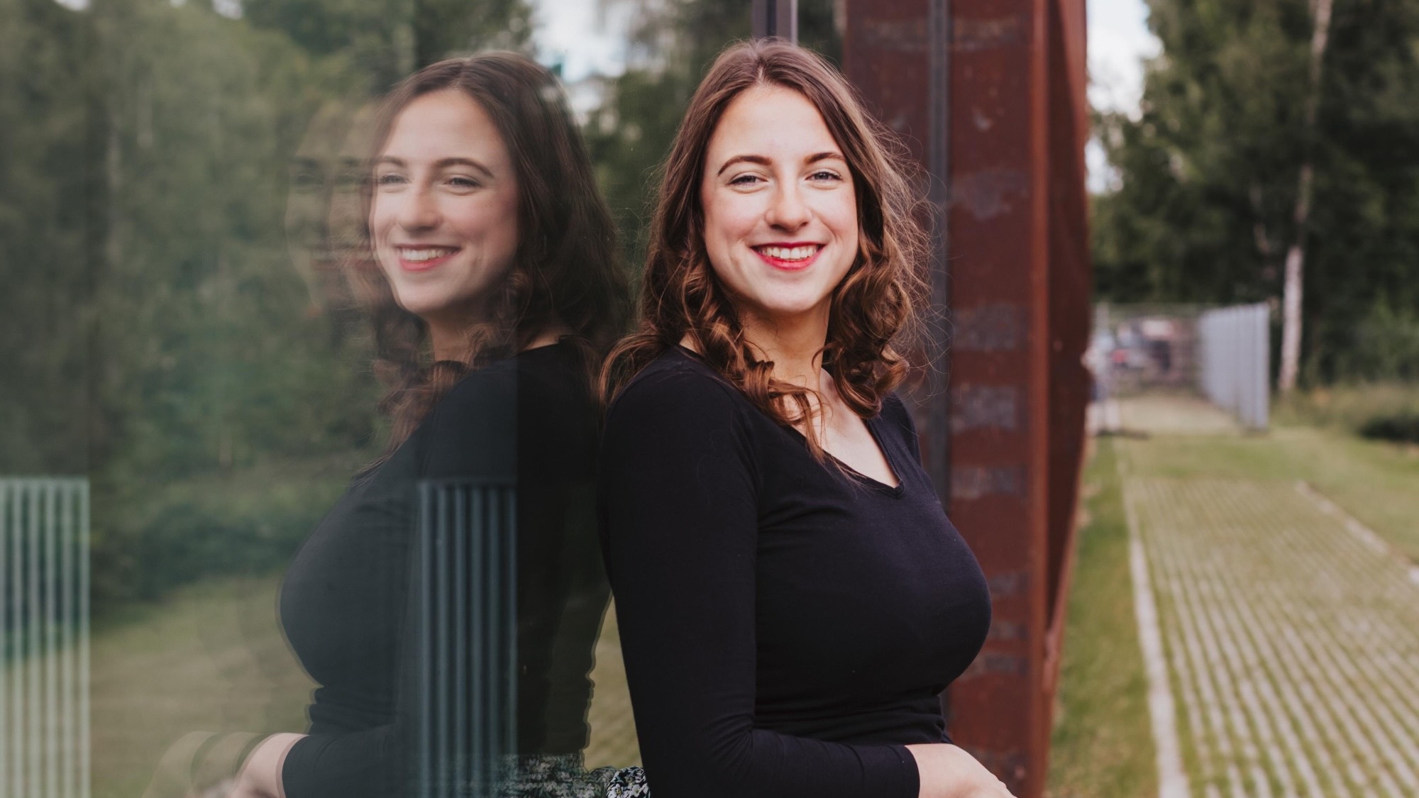 Pauline Fischer is leaning against a glass pane and smiling at the camera.