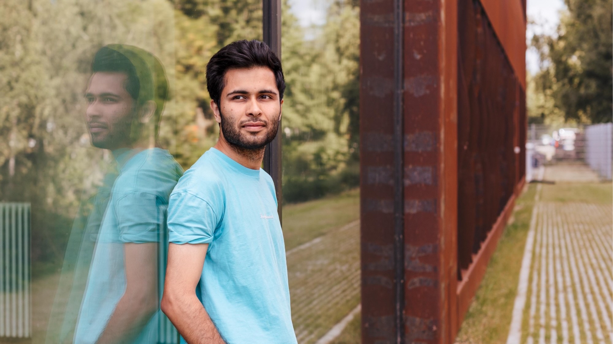 Muhammad Ahmed lehnt gegen ein Glasgebäude und schaut in die Ferne.