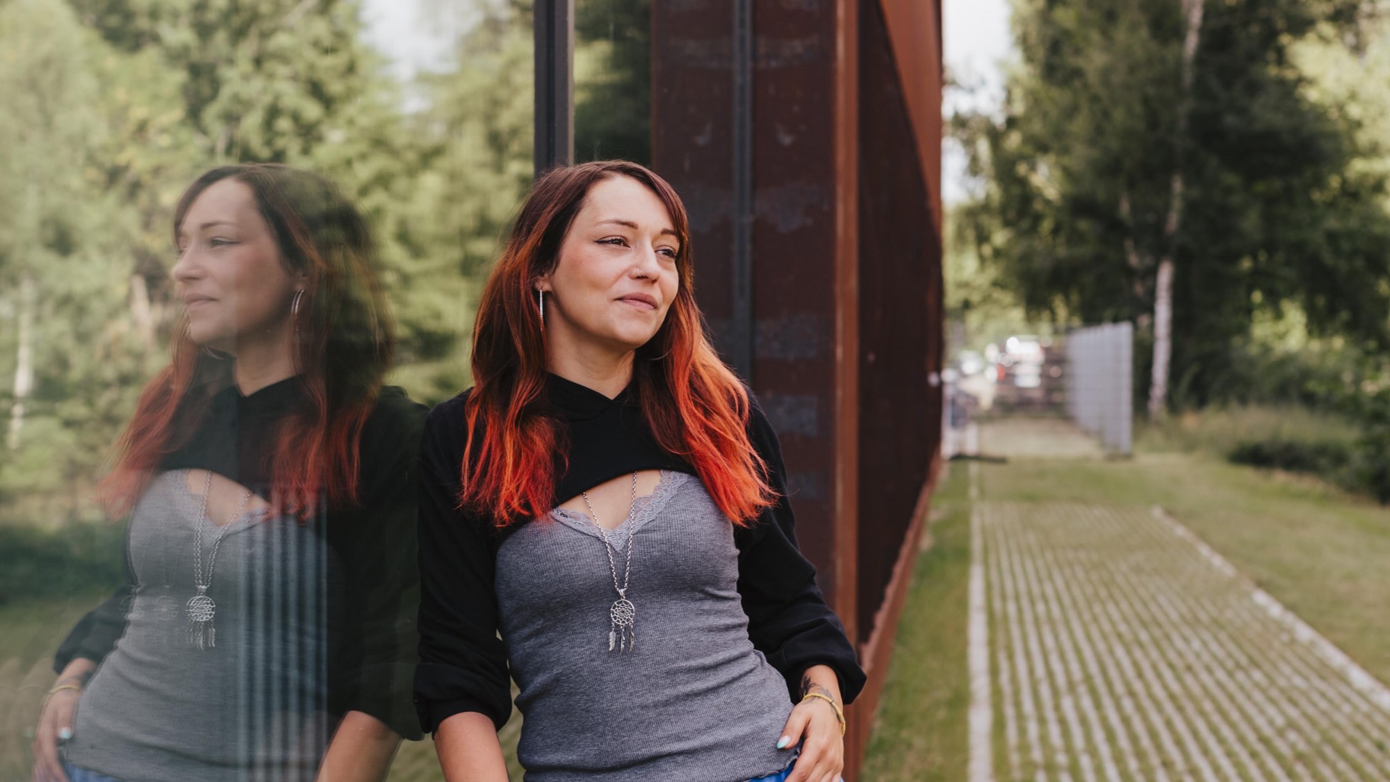 Jasmin Lanz lehnt gegen ein Glasgebäude und schaut in die Ferne.