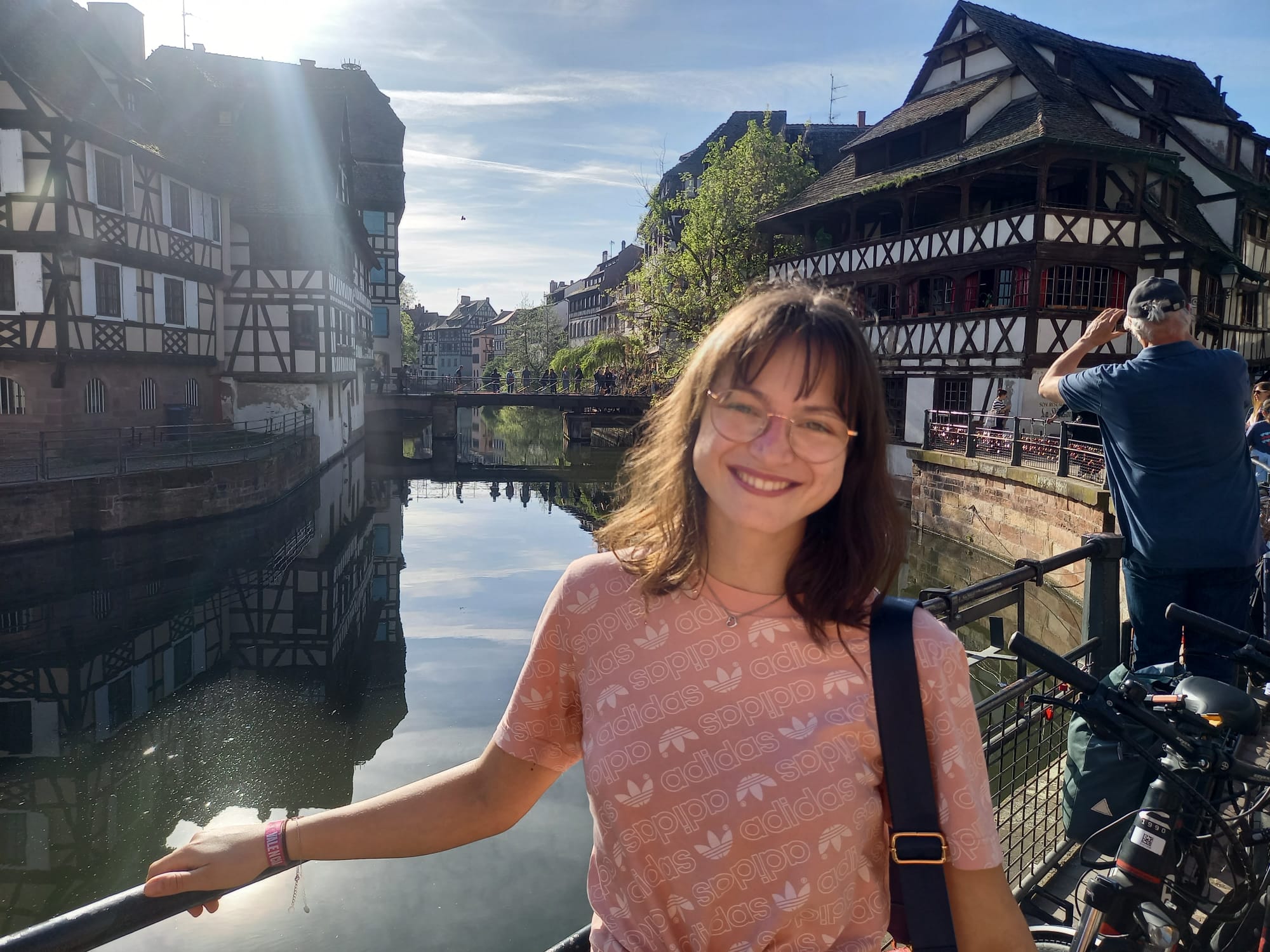 Eine junge Frau steht auf einer Brücke vor einem Fluss, der durch eine Reihe Fachwerkhäuser fließt.