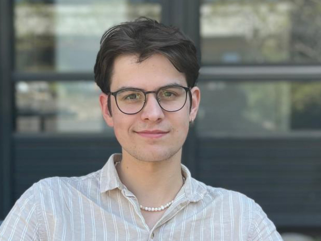 Ein junger Student mit Brille lächelt in die Kamera.