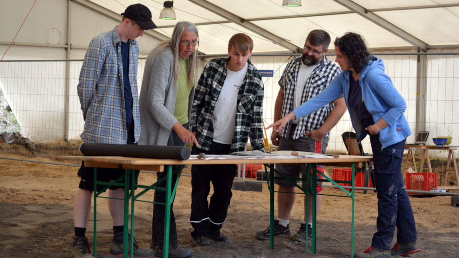 Uta Halle steht mit ihrem Team um einen Tisch herum an der Ausgrabungsstätte