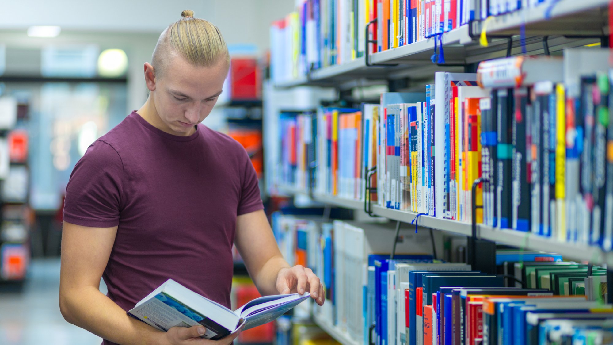 A person stands in front of a bookshelf and looks at a book. 