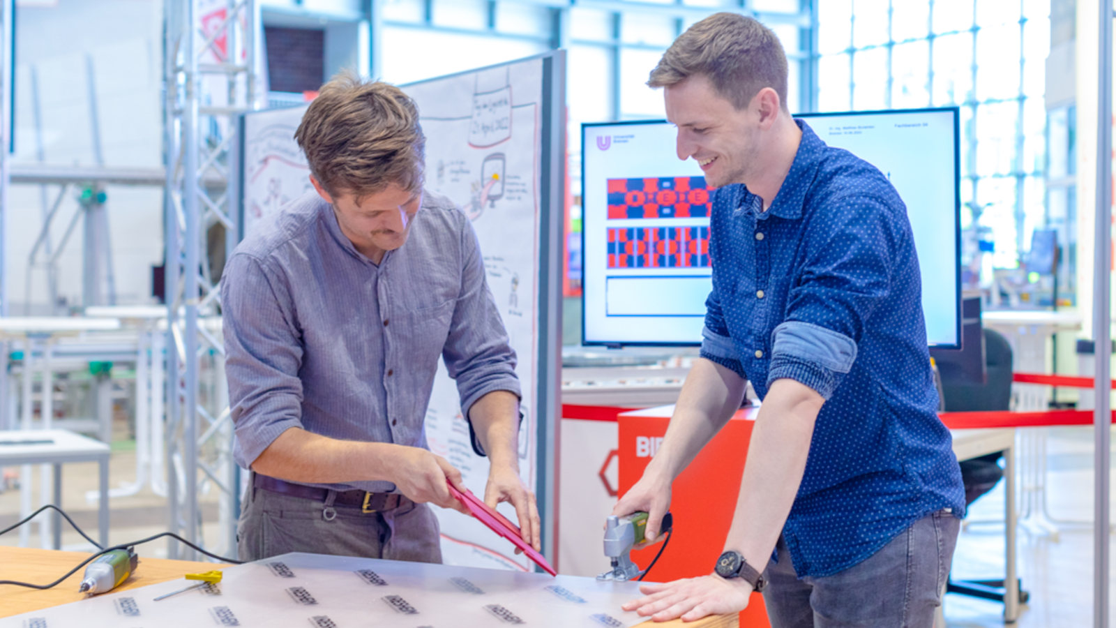 Matthias Burwinkel und Jonas Hörnschemeyer stehen mit Werkzeug an einem Tisch