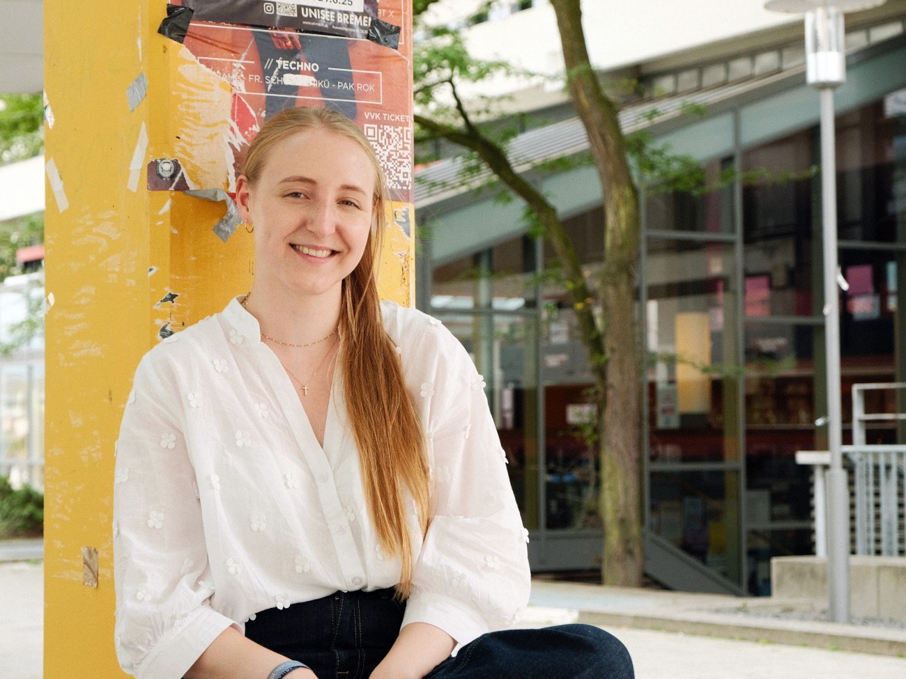 Eine Frau sitzt gegen eine gelbe Stütze gelehnt.