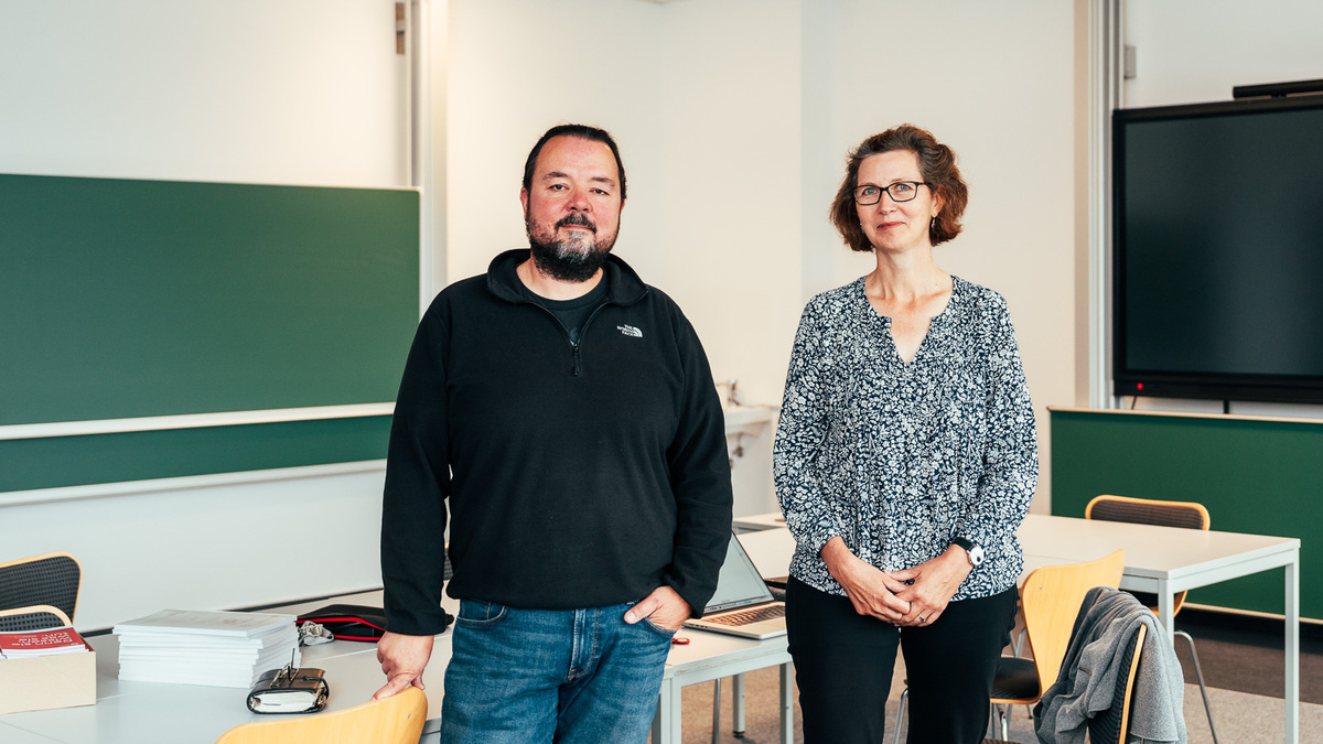 Professors Callies and Knipping are standing in the didactics lab in front of the teacher’s desk; in the background are green chalkboards.