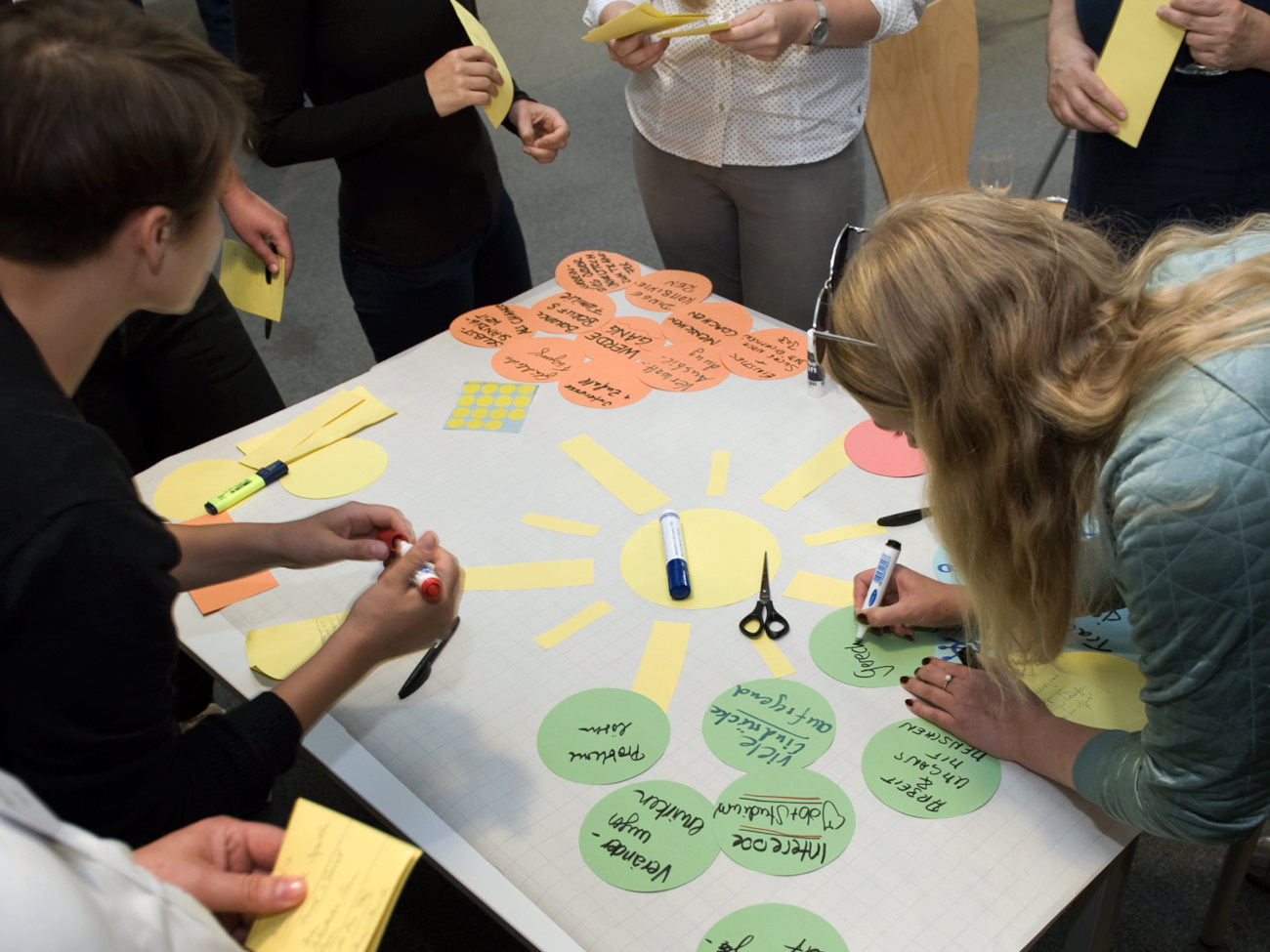 People stand around a table and write words on colorful notepads