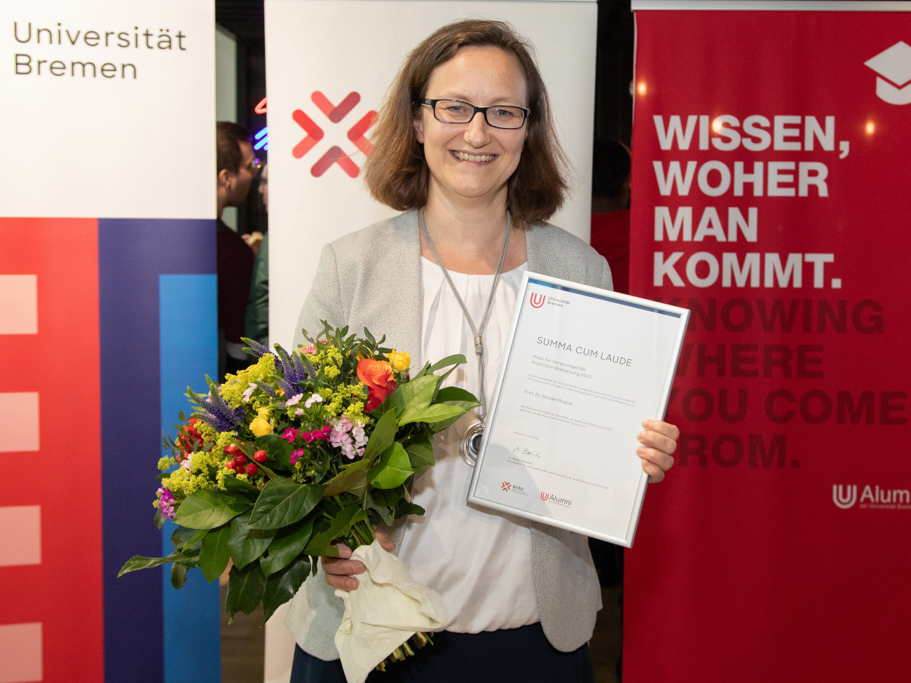 Nicole Megow mit einem Blumenstrauß in der einen und dem Zertifikat für herausragende Promotionsbetreuung in der anderen Hand.