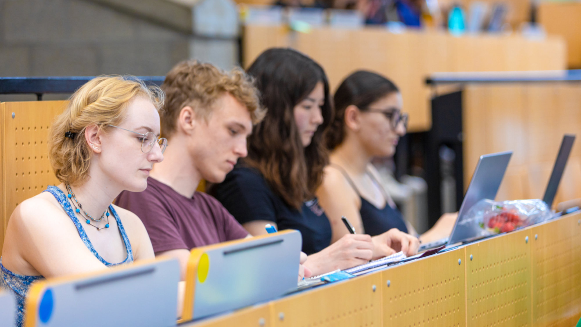 Four students sitting in a lecture hall and working at their computers.