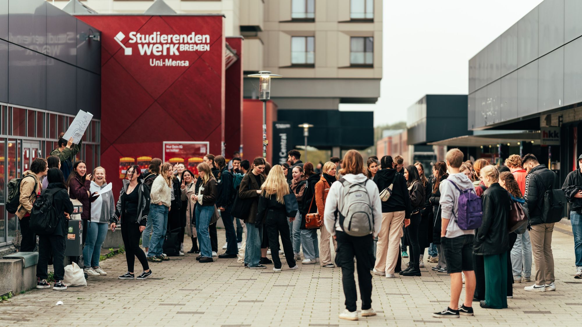 Menschen stehen in einem Halbkreis. Eine Person hält ein Schild hoch.