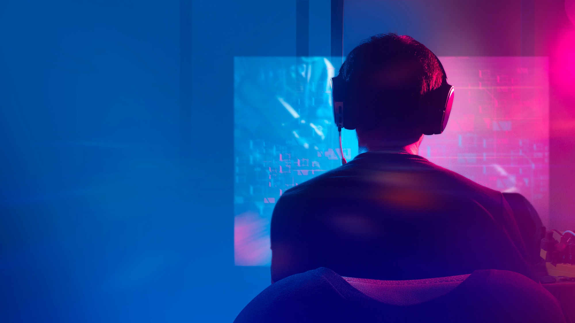The picture shows the back of a person sitting in front of a computer wearing a headset.