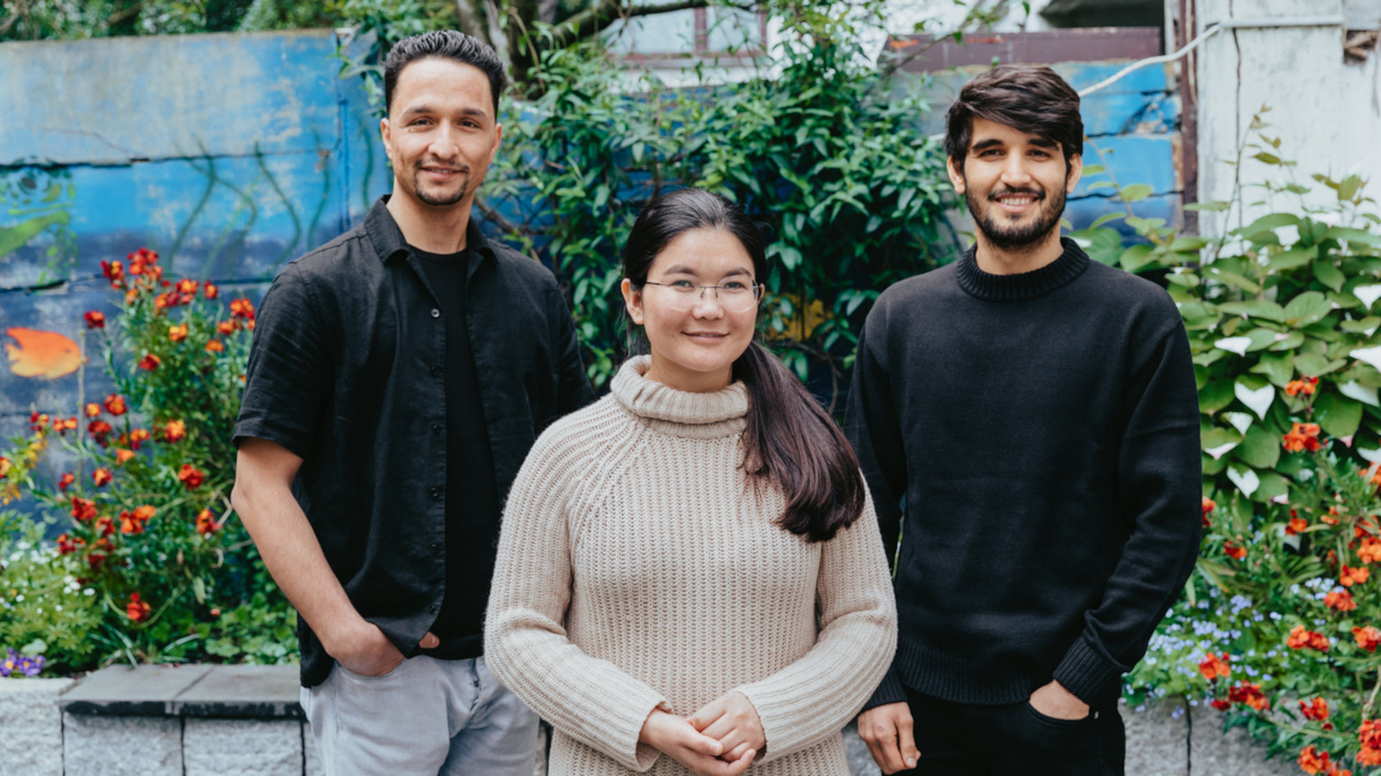 Sohrab Zarbafiyan, Nazdana Sultanfar und Mohammad Fahim Amini stehen draußen vor einem Hintergrund, in dem Pflanzen zu sehen sind.