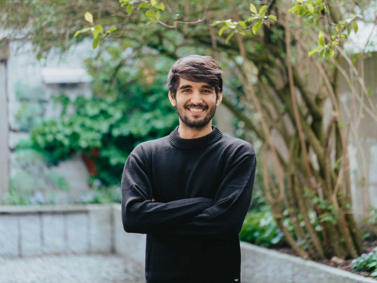Mohammad Fahim Amini stands outside and smiles at the camera. Plants and a small stone wall can be seen in the background.