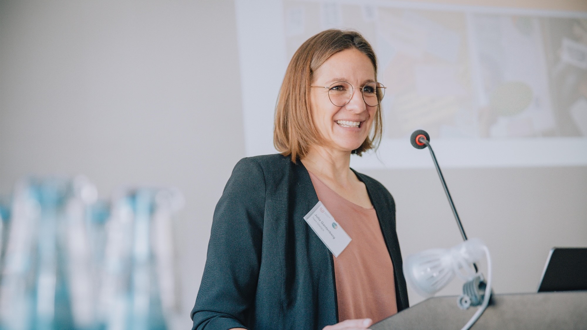 A photo of Julia Gantenberg standing at a speaker's podium with a smile on her face.